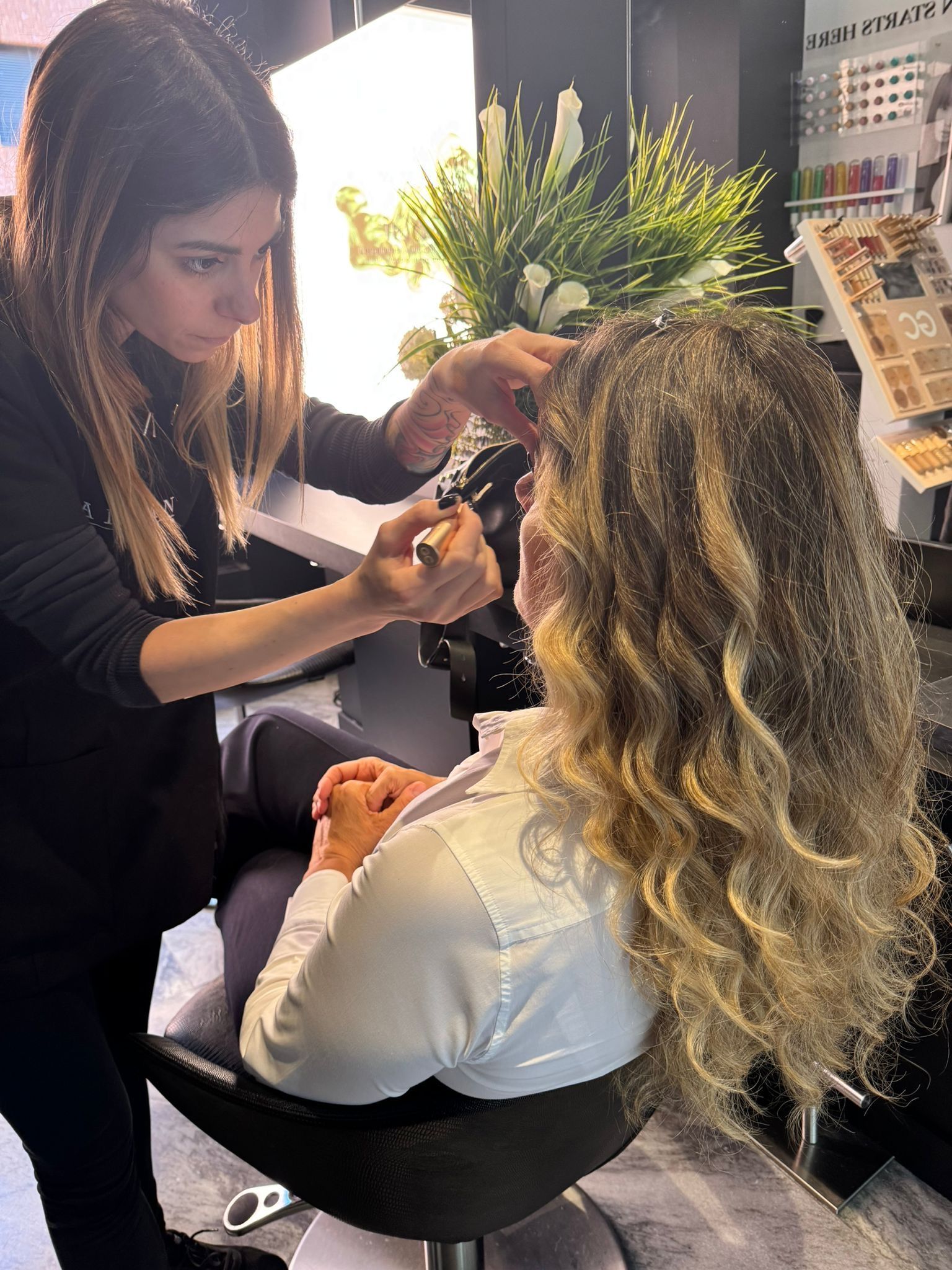 Una truccatrice professionista applica il trucco a una persona con capelli lunghi, ricci e con mèches in un salone di bellezza.