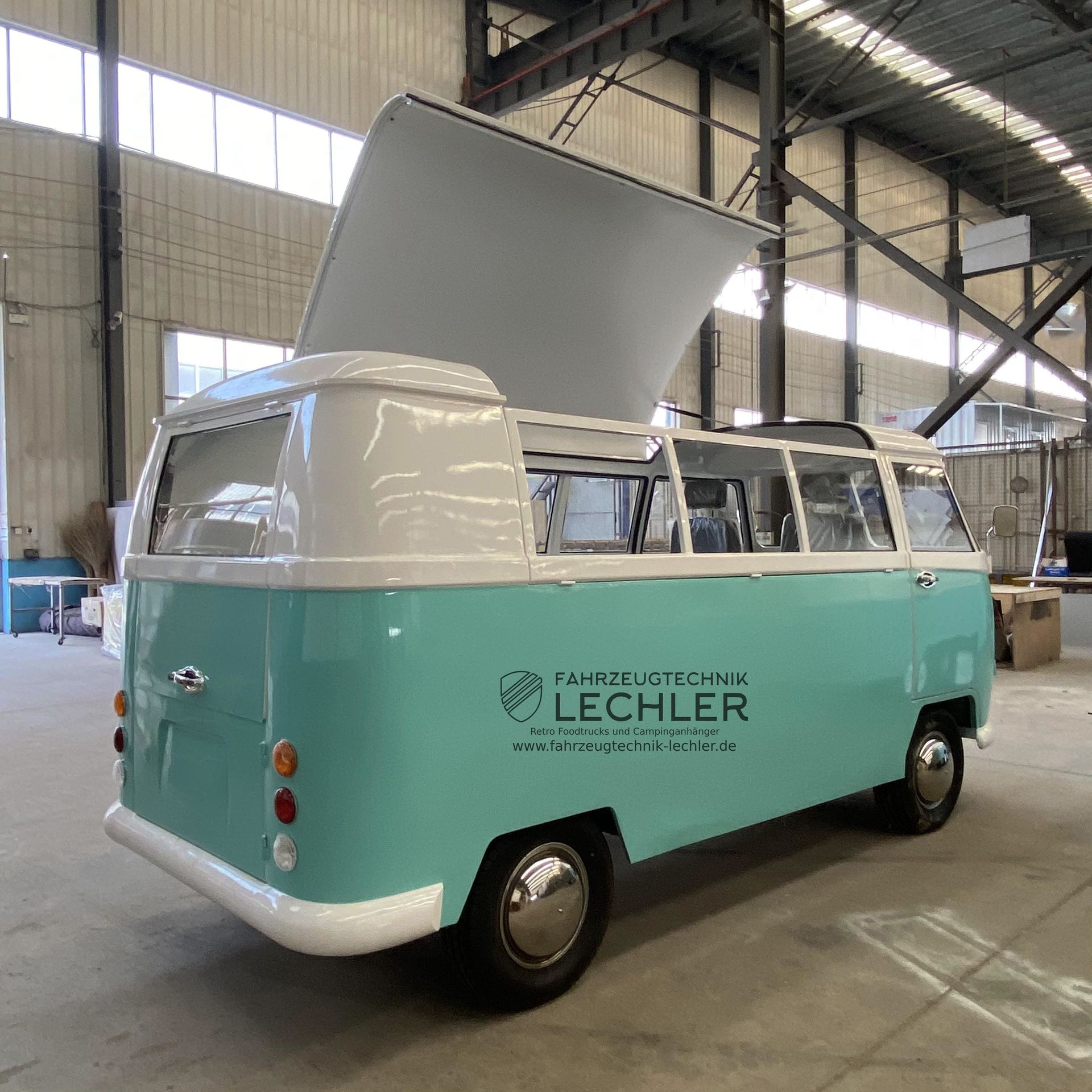 Türkis-weißer VW-Oldtimerbus, Rückansicht, mit geöffnetem Dach, in einer Lagerhalle.