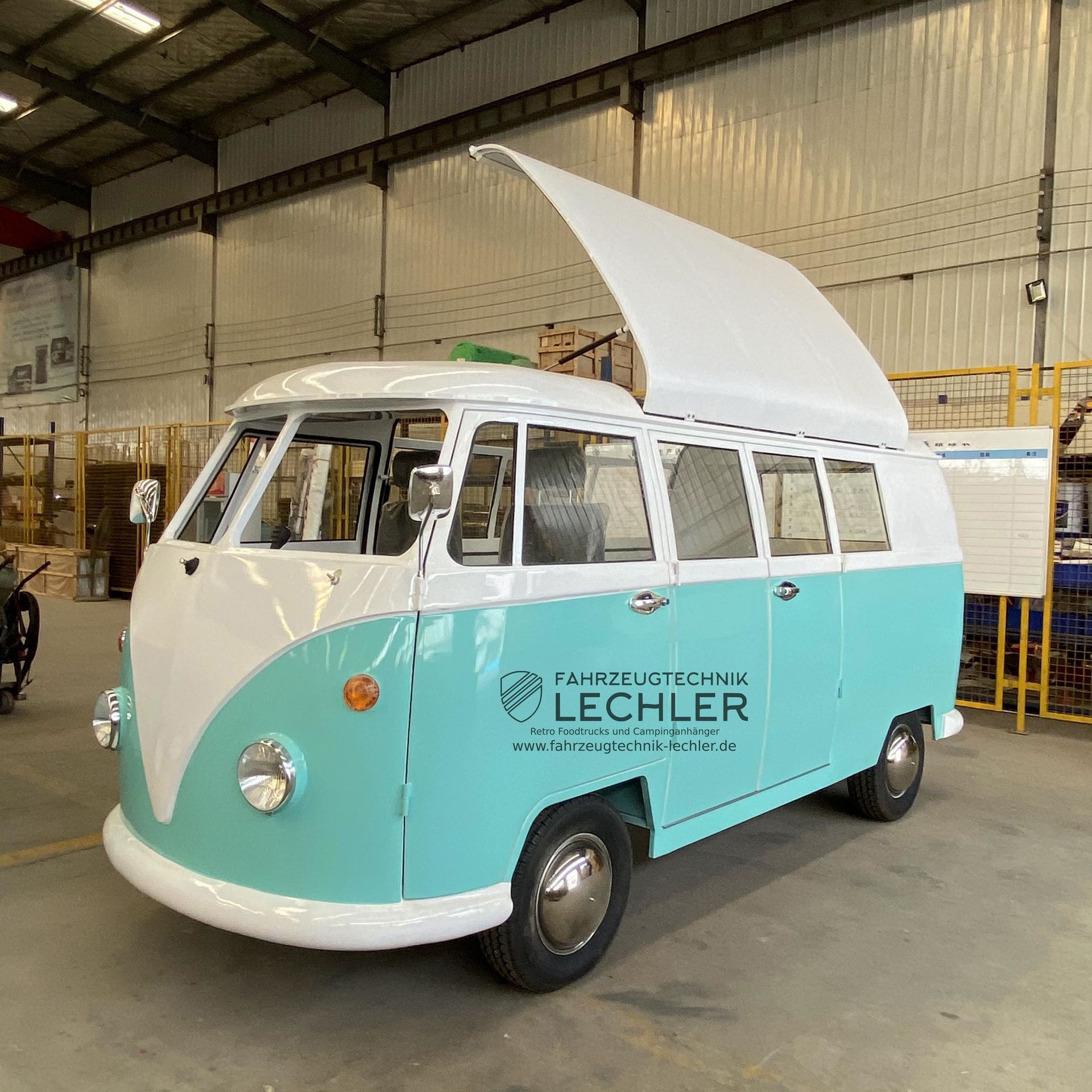 Hellblauer und weißer VW-Bus mit offenem Dachaufsatz in einer Lagerhalle.
