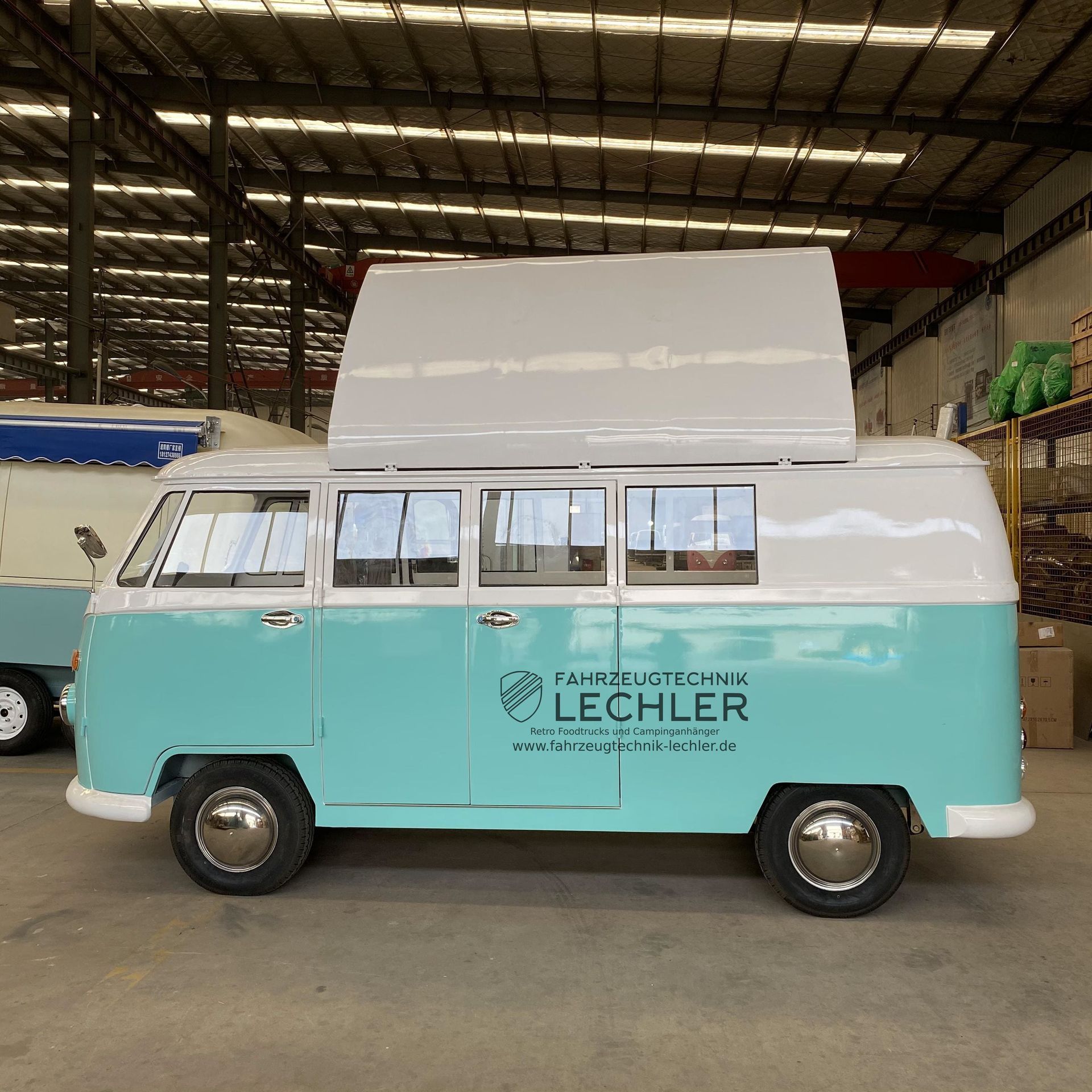 Türkis-weißer Imbisswagen mit aufklappbarem Dach, in einer Halle geparkt. Mit „LECHLER“-Logo an der Seite.