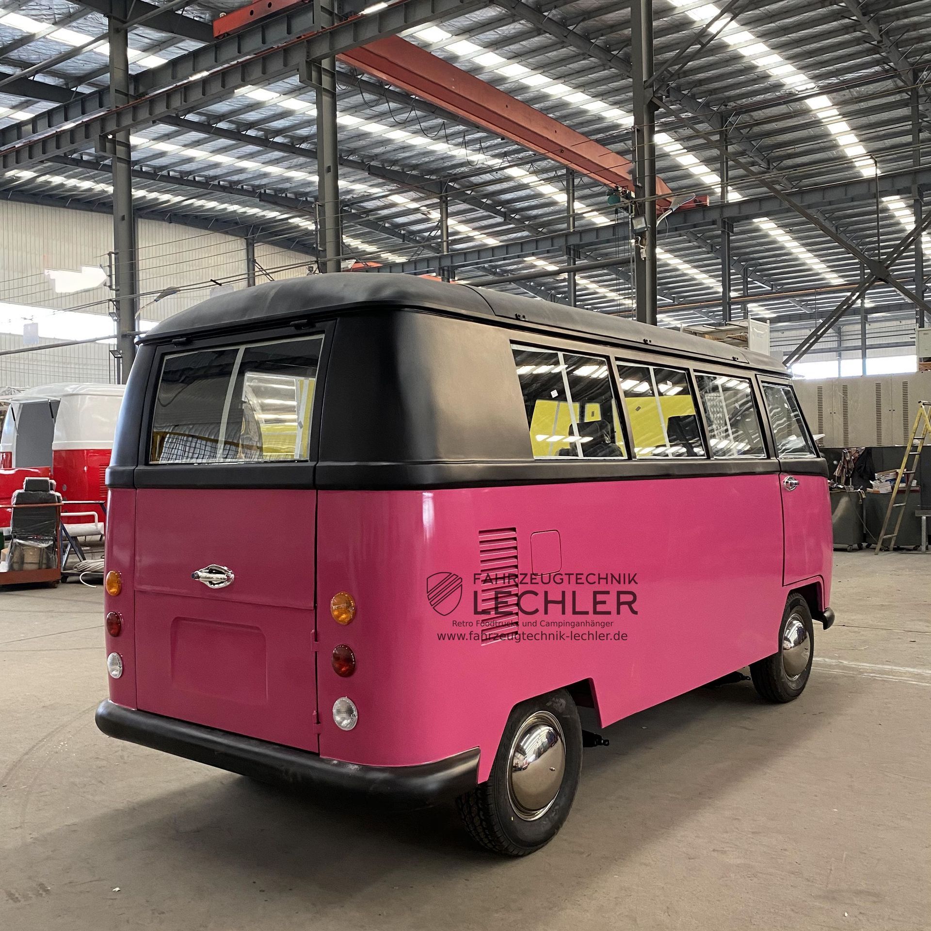 Ein rosafarbener und schwarzer VW-Bus in einem Industriegebiet.