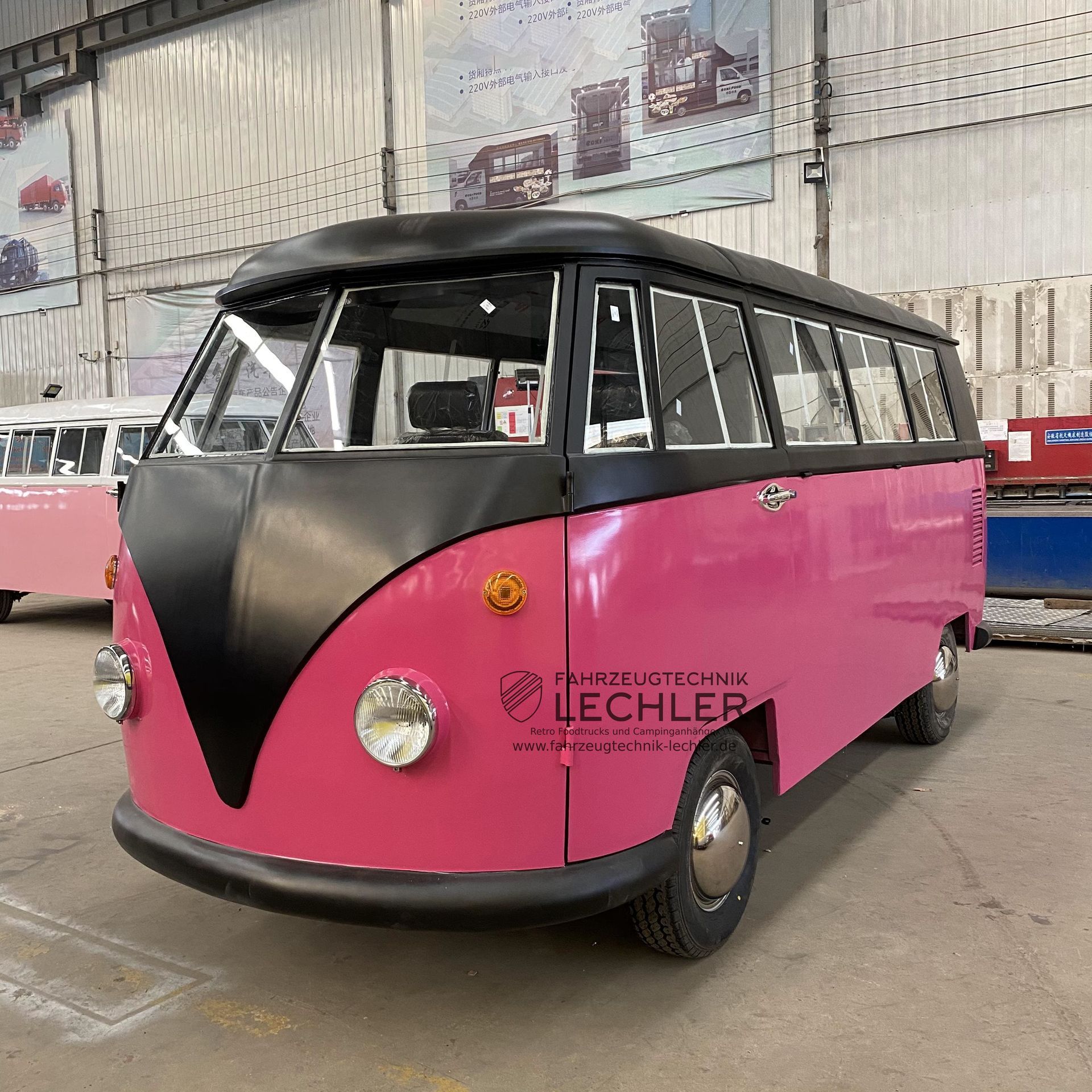 Ein rosafarbener und schwarzer VW-Oldtimerbus in einer Fabrikumgebung.