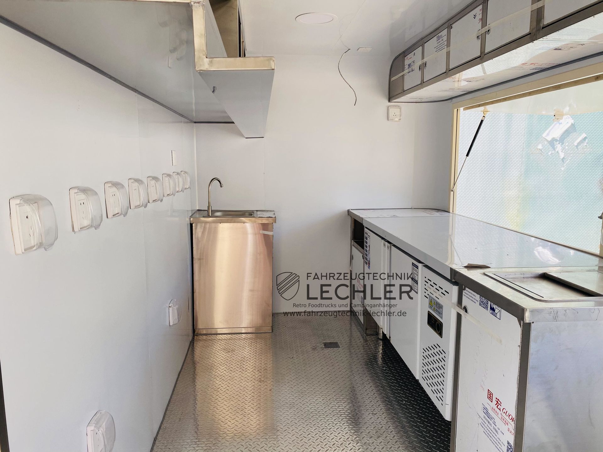 Innenraum eines leeren Imbisswagens aus Edelstahl: Spülbecken, Arbeitsflächen, Schränke und Steckdosen an der Wand.