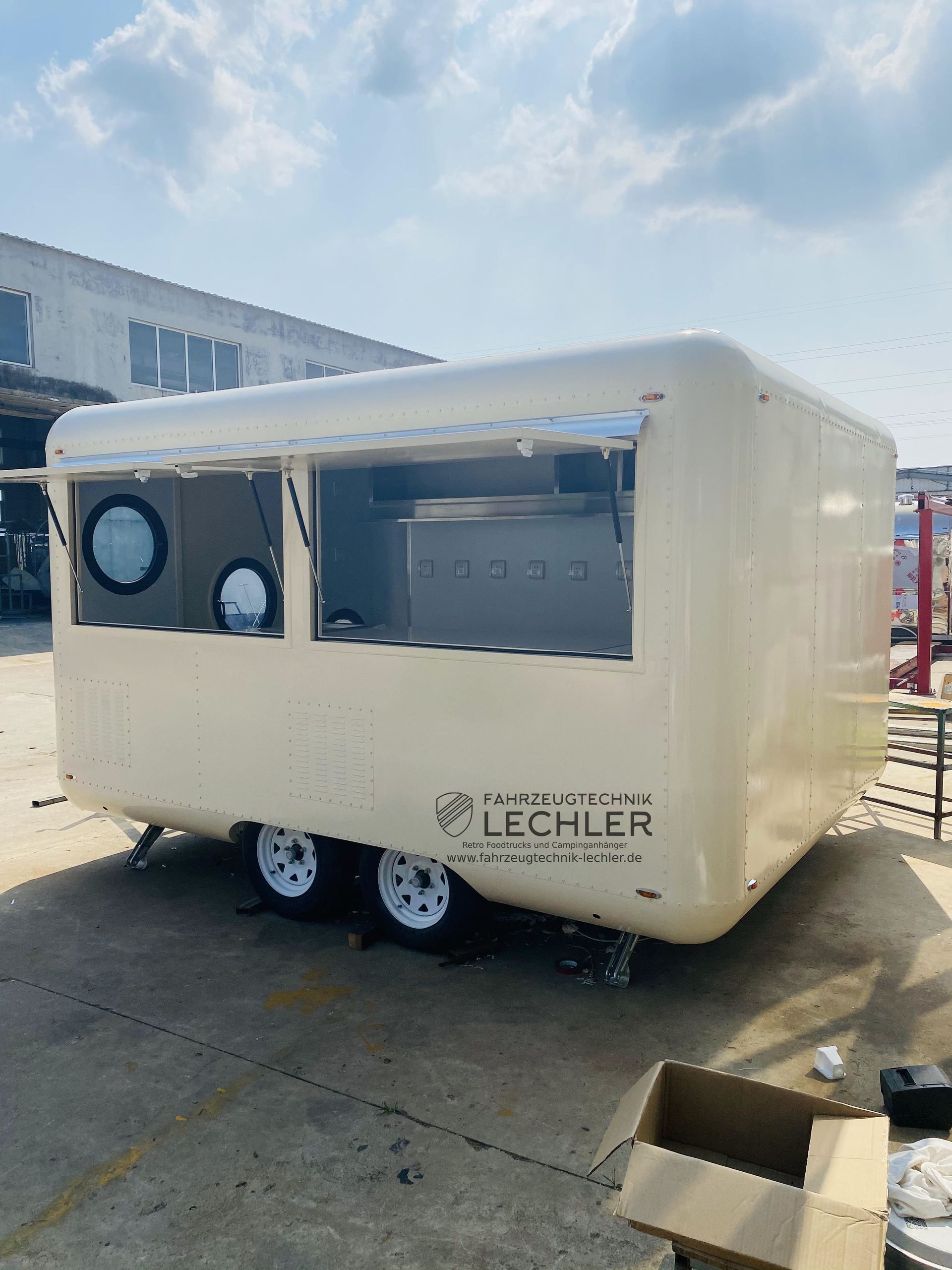 Cremefarbener Imbisswagen mit großem Ausgabefenster und rundem Bullauge. „LECHLER“-Logo an der Seite.