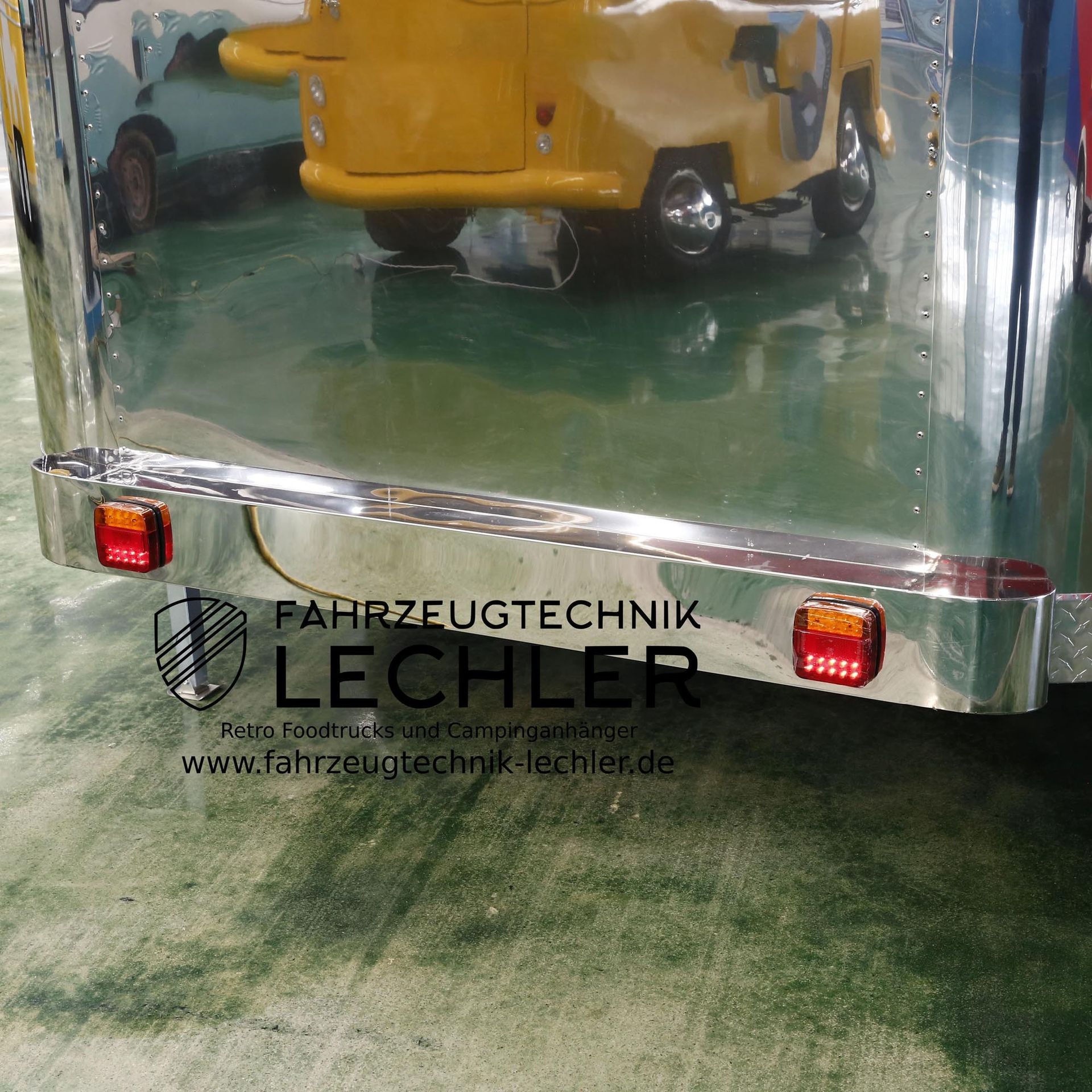 Rückansicht eines glänzenden, chromähnlichen Anhängers mit roten Lichtern und einem gelben Fahrzeug, das sich in der Oberfläche spiegelt.