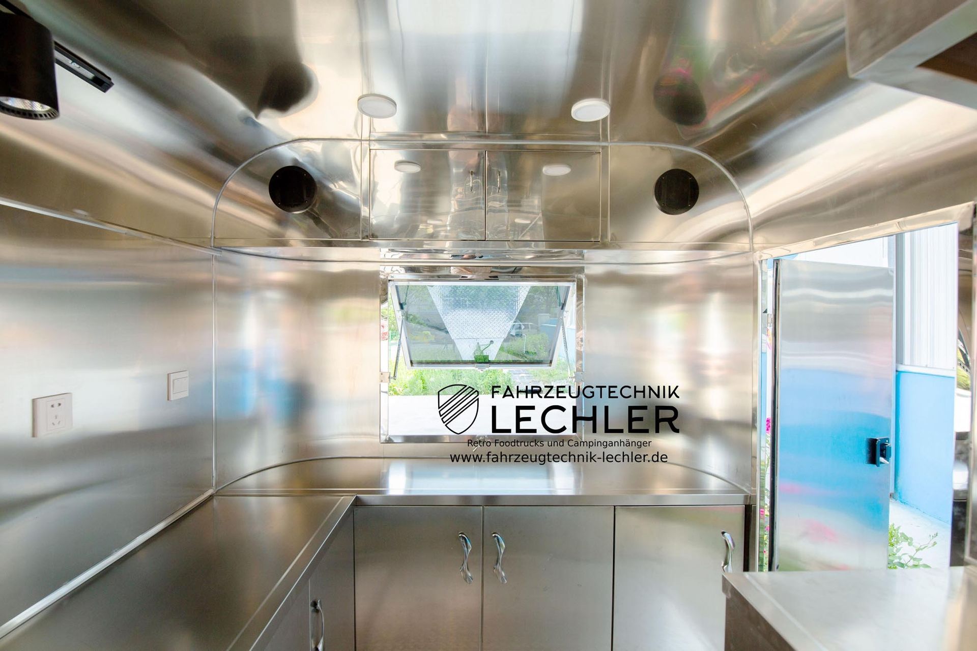 Innenansicht eines glänzenden Edelstahl-Anhängers mit Theke, Schränken und Fenster. Das Logo „Lechler“ ist sichtbar.