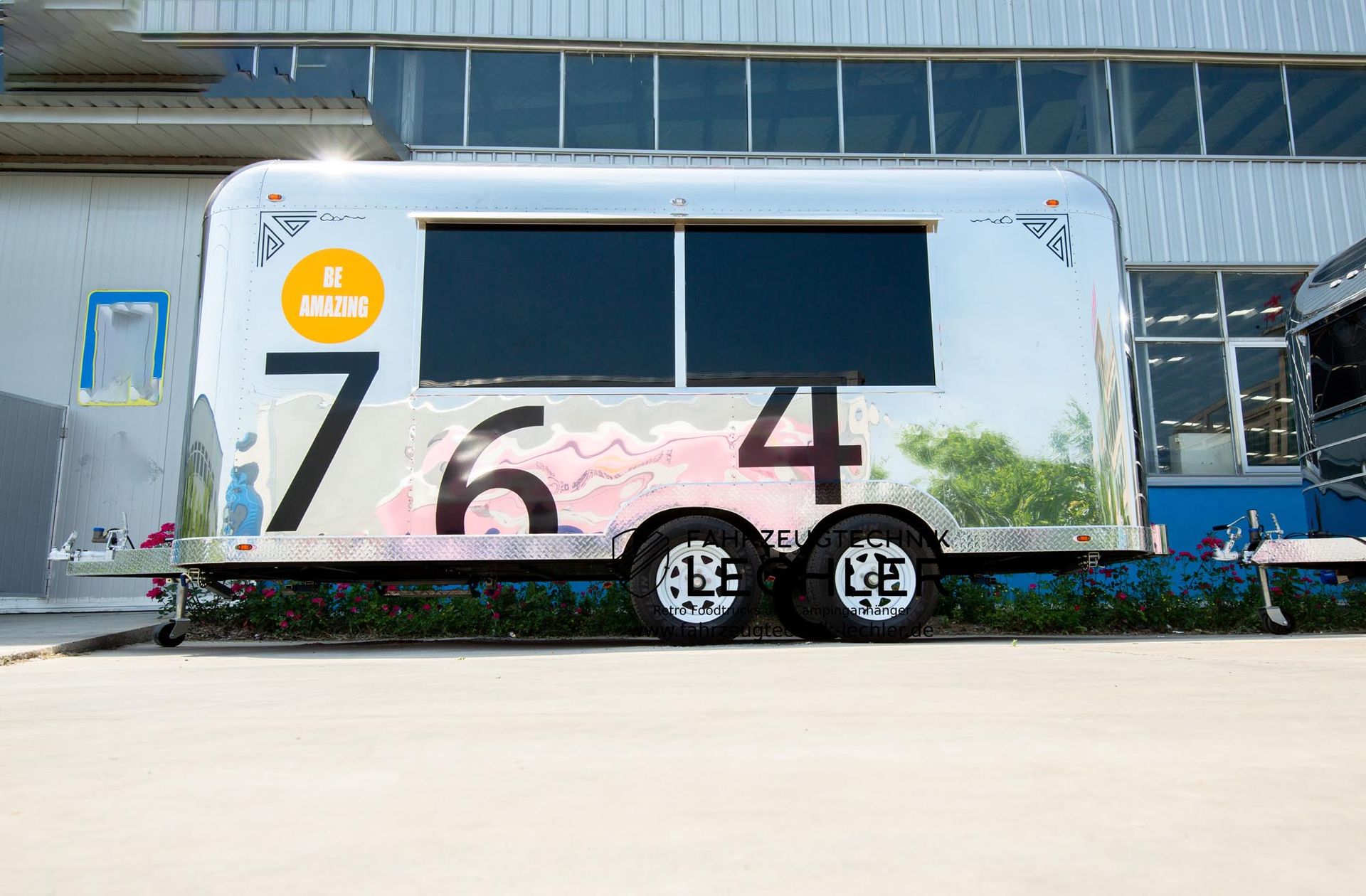 Ein glänzender, silberner Imbisswagen mit großen schwarzen Ziffern „764“ an der Seite, in der Nähe eines Gebäudes.