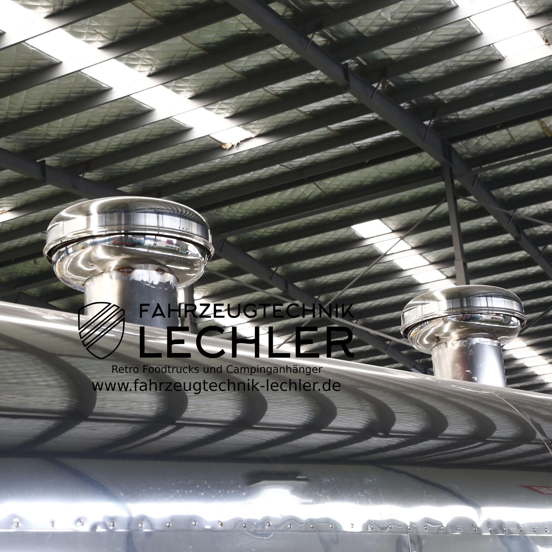 Zwei silberne Dachlüfter auf einem Wellblechdach unter der Decke einer Lagerhalle.