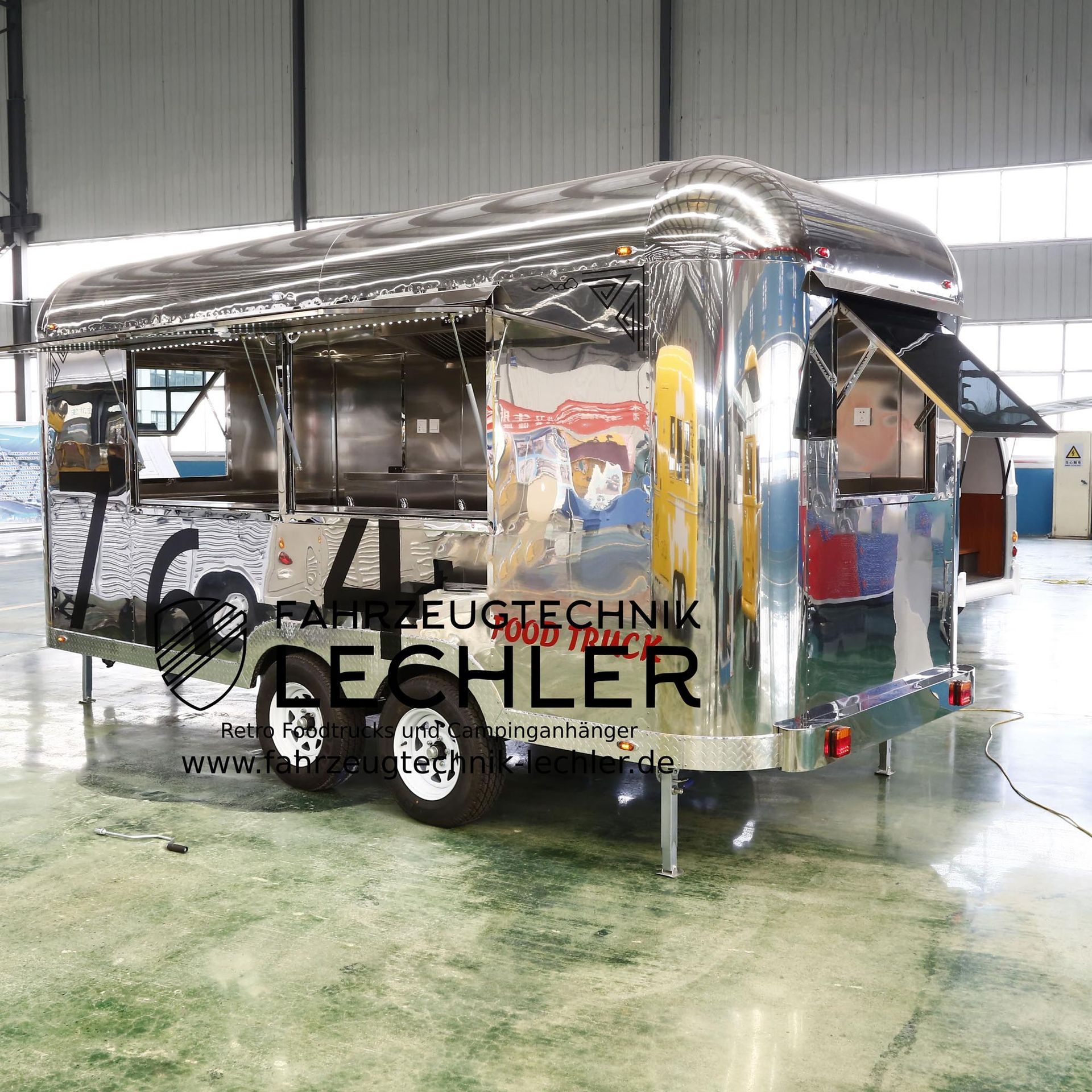 Ein glänzender, silberner Imbisswagen mit offenen Ausgabefenstern, der in einem Gebäude geparkt ist.