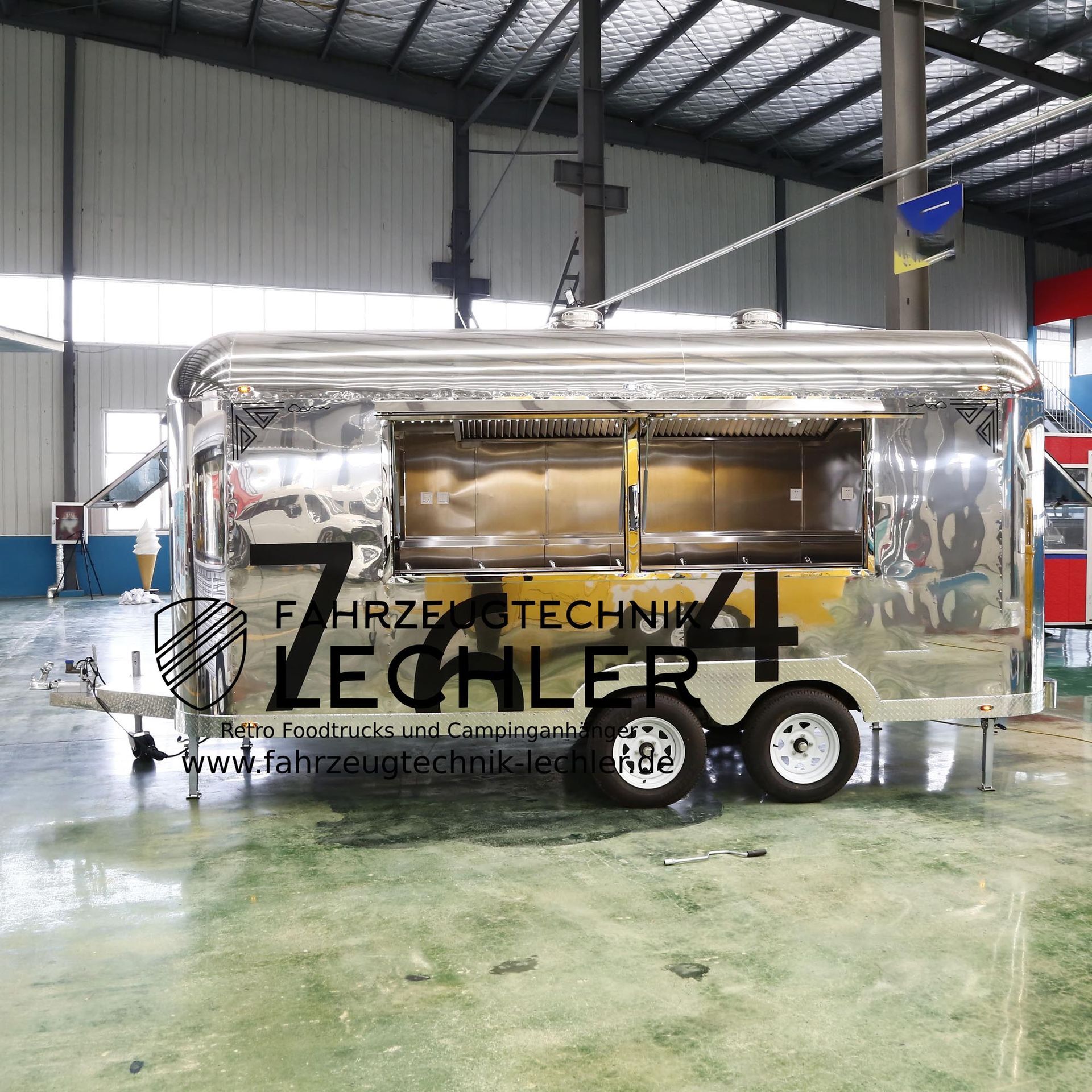 Ein glänzend silberner Imbisswagen mit großem Ausgabefenster, der in einer großen Werkstatt parkt.