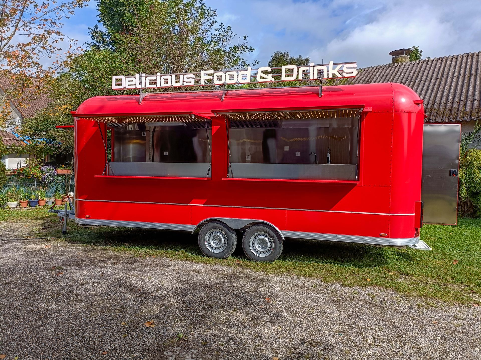 Roter Imbisswagen mit dem Schild „Delicious Food & Drinks“, zwei Ausgabefenstern und einer Tür aus Edelstahl, draußen geparkt.