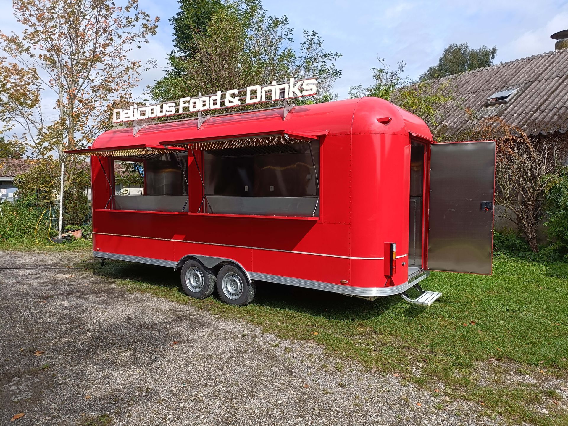 Roter Imbisswagen mit offenen Ausgabefenstern, Tür und dem Schild „Leckeres Essen & Getränke“.
