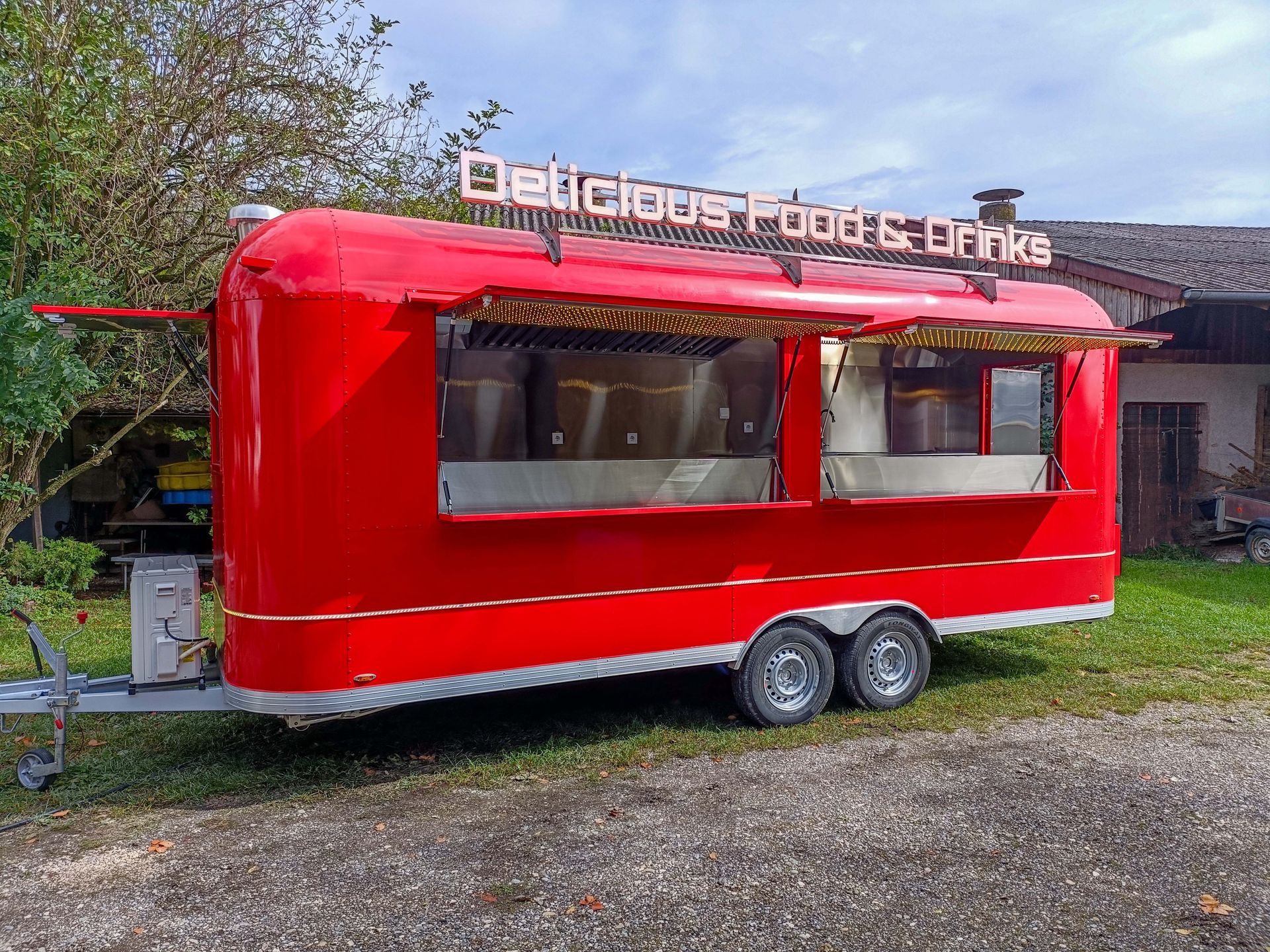 Roter Imbisswagen mit der Aufschrift „Leckeres Essen & Getränke“, geparkt auf einer Rasenfläche.