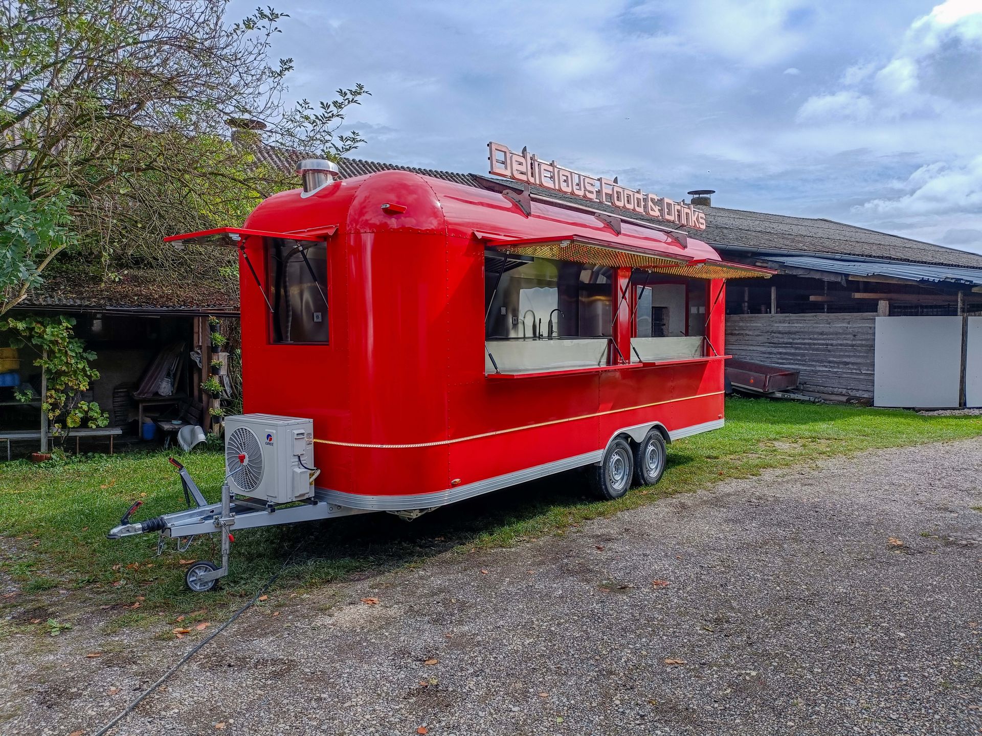 Roter Imbisswagen mit Markise auf einer Rasenfläche, im Hintergrund ein Gebäude.