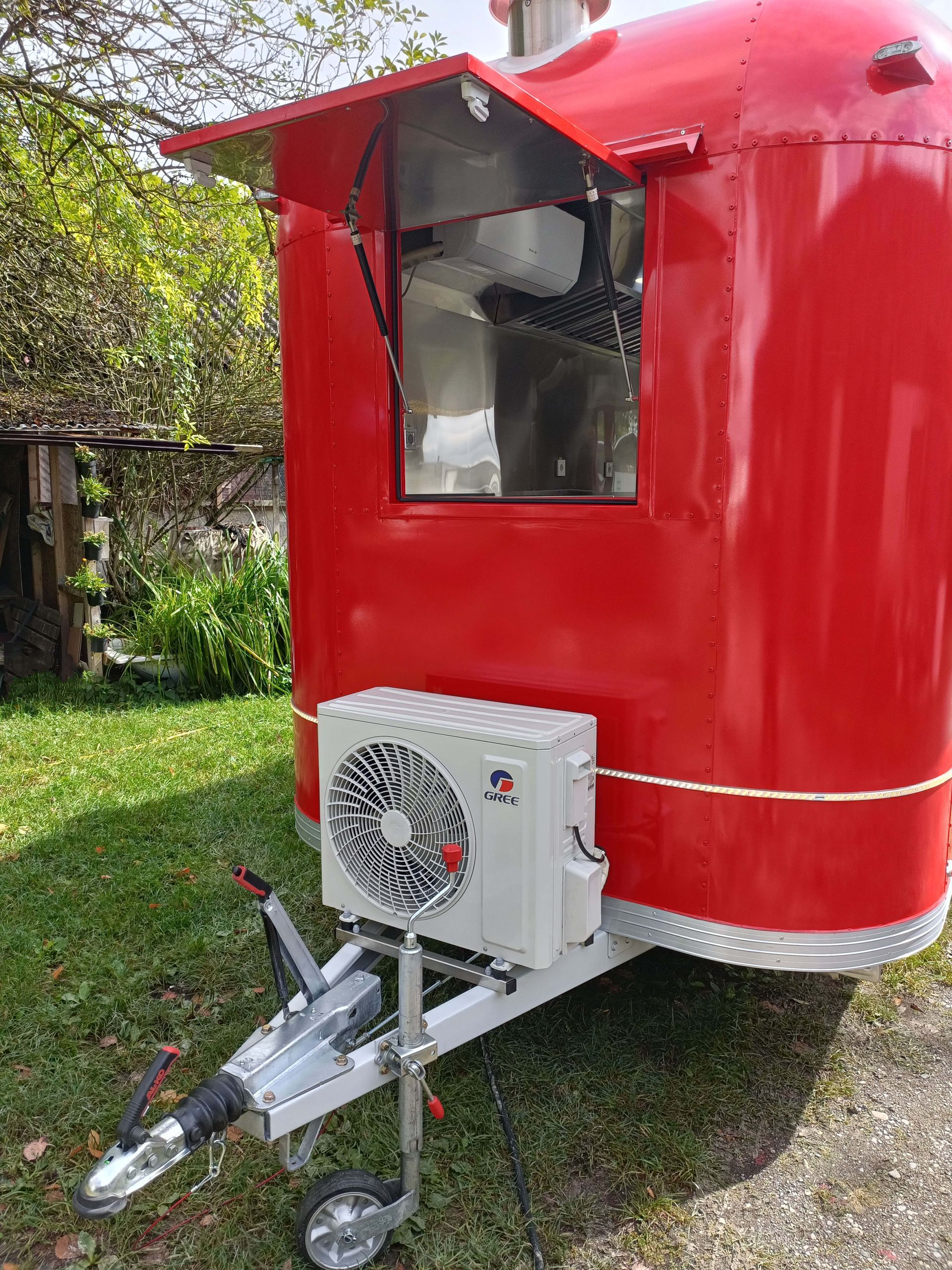 Roter Imbisswagen mit angebauter Klimaanlage, geparkt auf einer Rasenfläche.