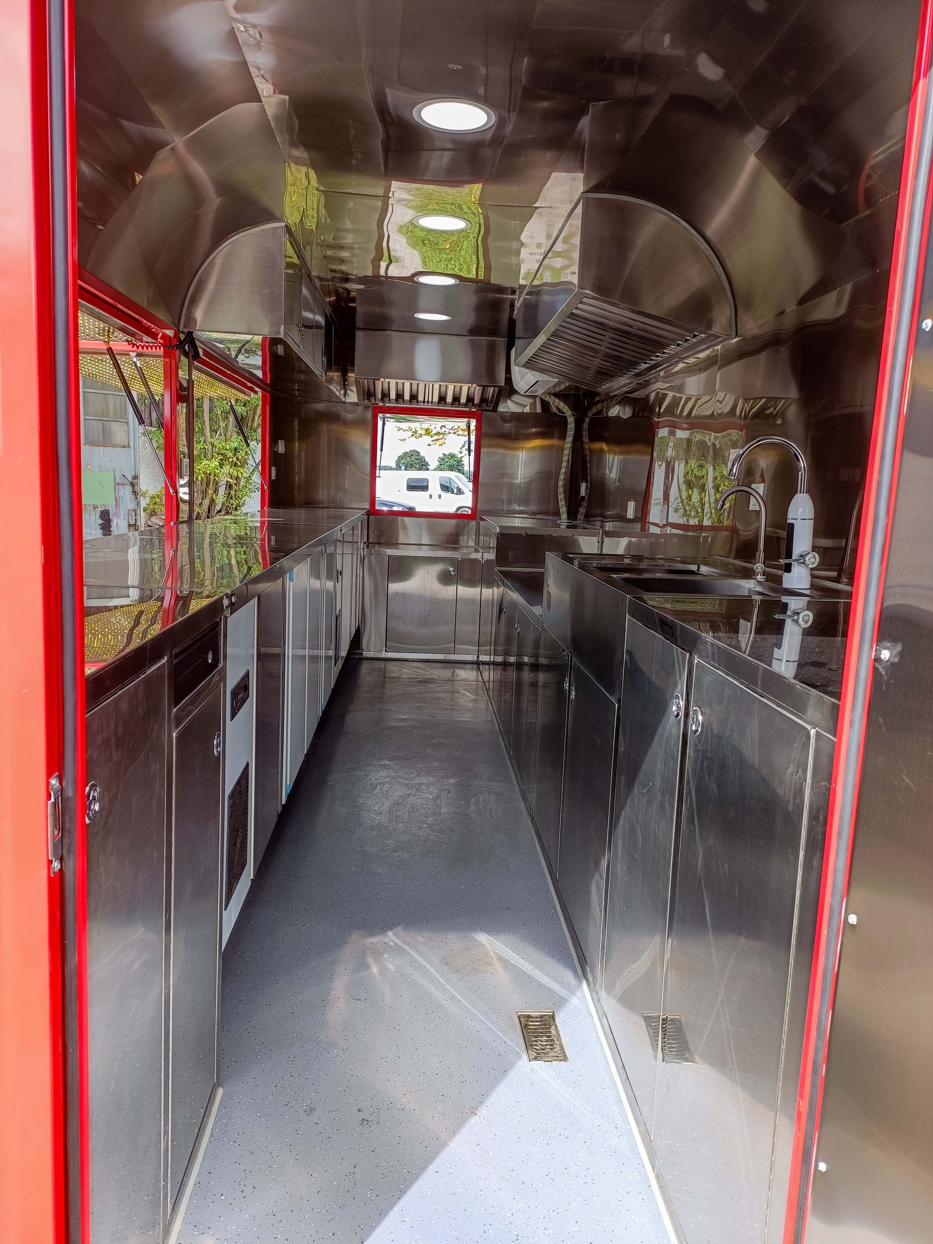 Innenraum eines roten Imbisswagens mit Theken und Geräten aus Edelstahl; leer.