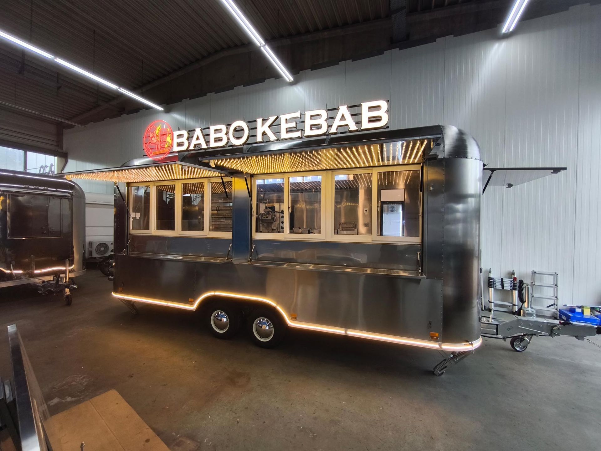 Imbisswagen mit dem Schild „BABO KEBAB“; Außenverkleidung aus Edelstahl, offene Ausgabefenster, beleuchtete Zierelemente.