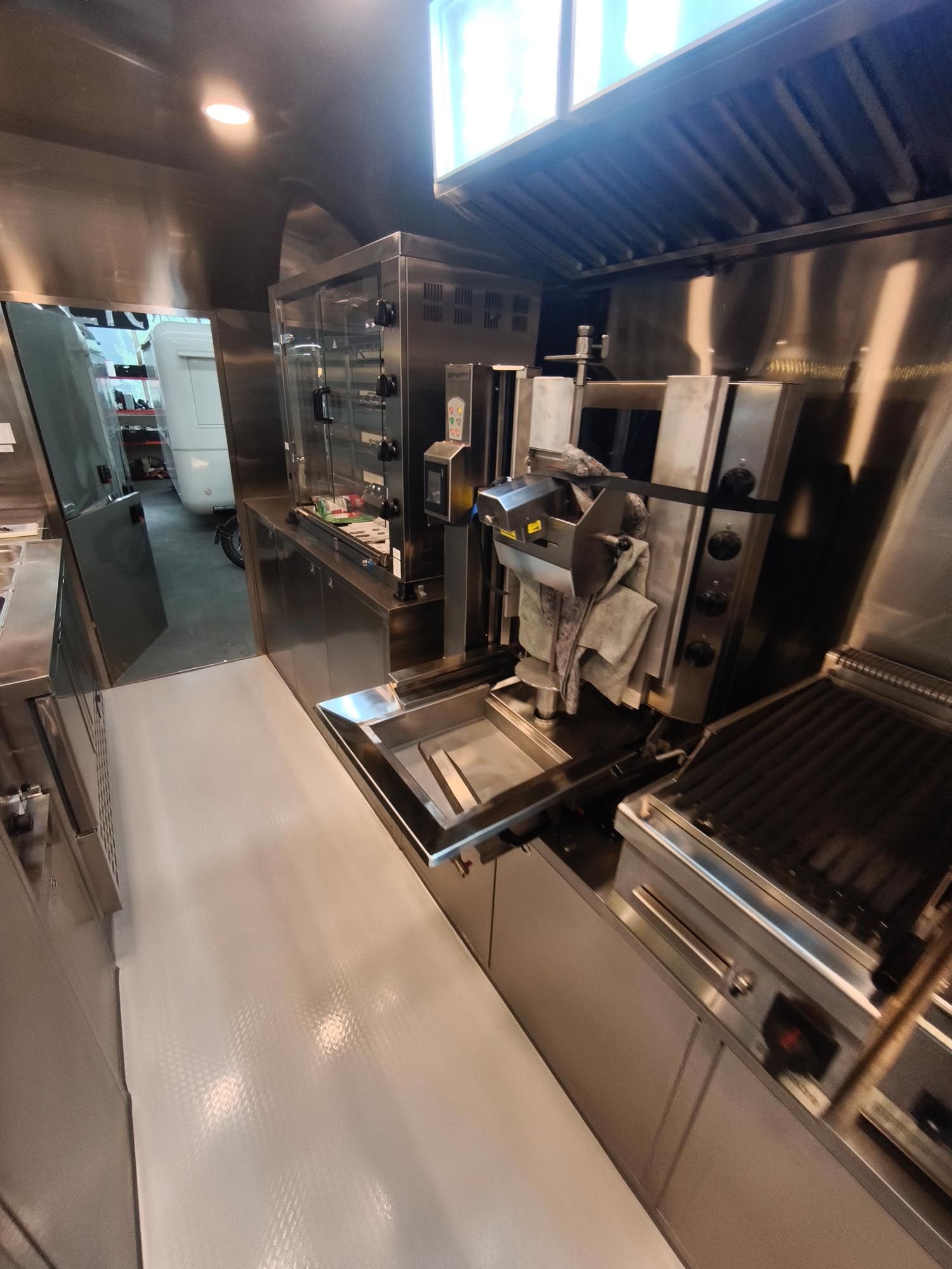 Innenansicht der Küche eines Imbisswagens mit vertikalem Drehspieß für Fleisch, Grill und Arbeitsflächen aus Edelstahl.