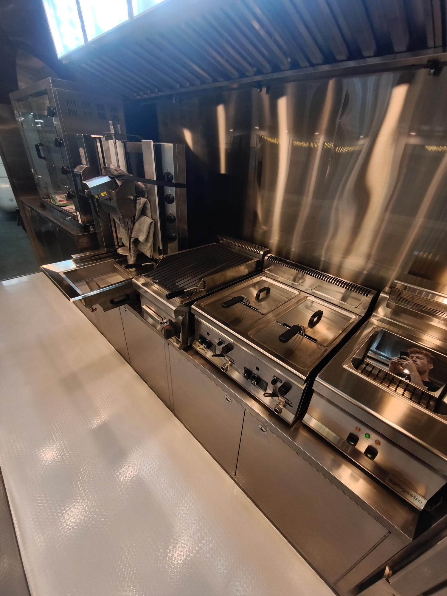 Küchengeräte aus Edelstahl, darunter Grills und Fritteusen, unter einer Dunstabzugshaube.