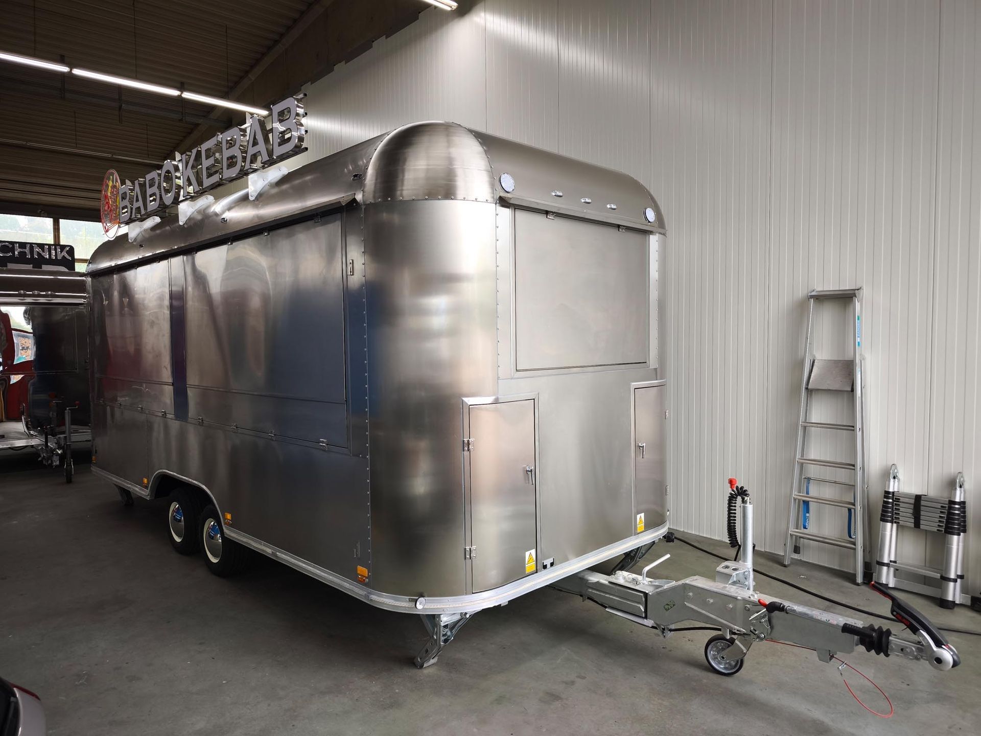 Glänzender silberner Imbisswagen mit dem Schild „DURUM KEBAB“; angekuppelt, in einer Halle geparkt.