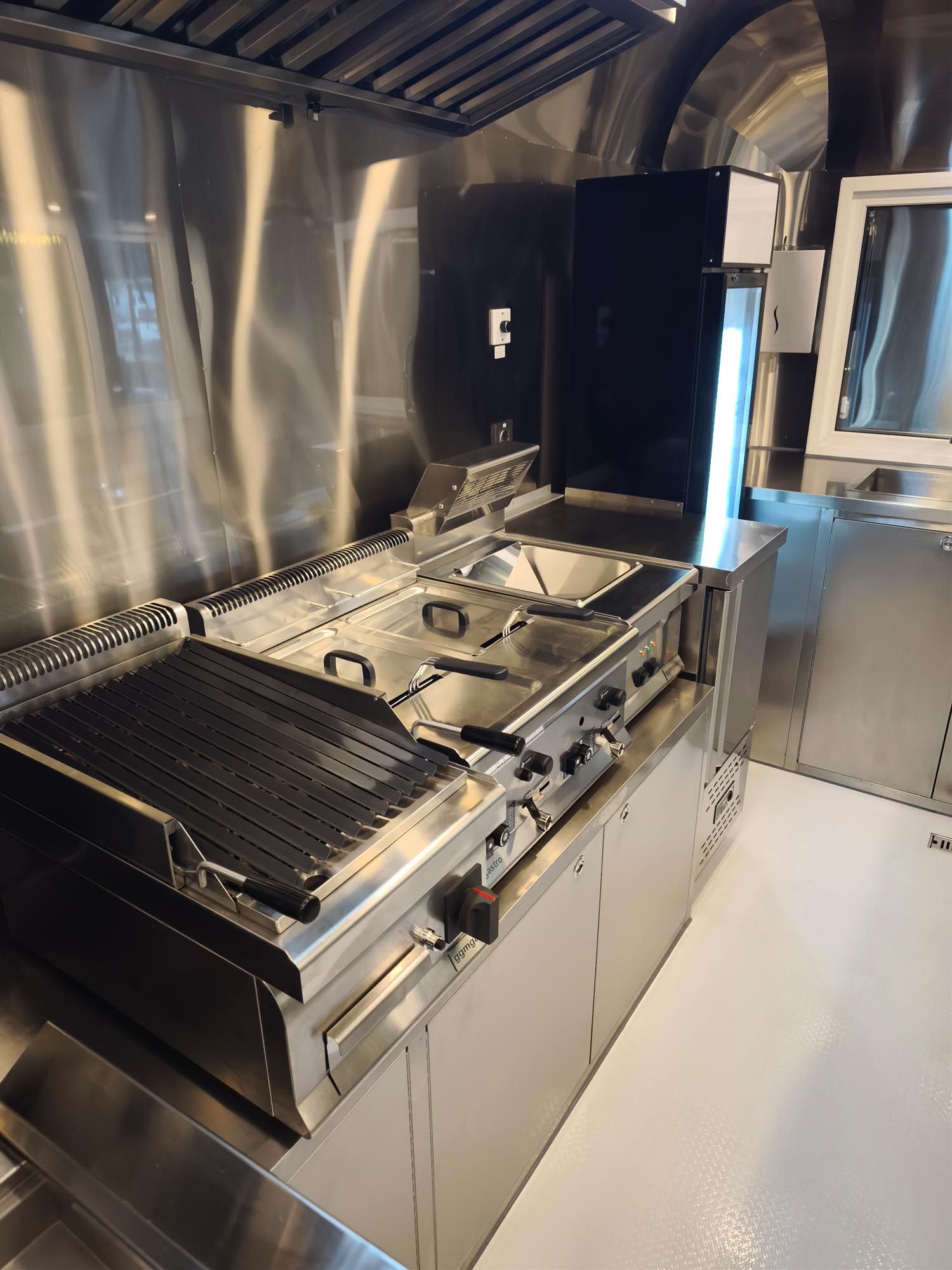 Innenraum der Imbisswagenküche aus Edelstahl mit Grill, Fritteusen und Dunstabzugshaube.