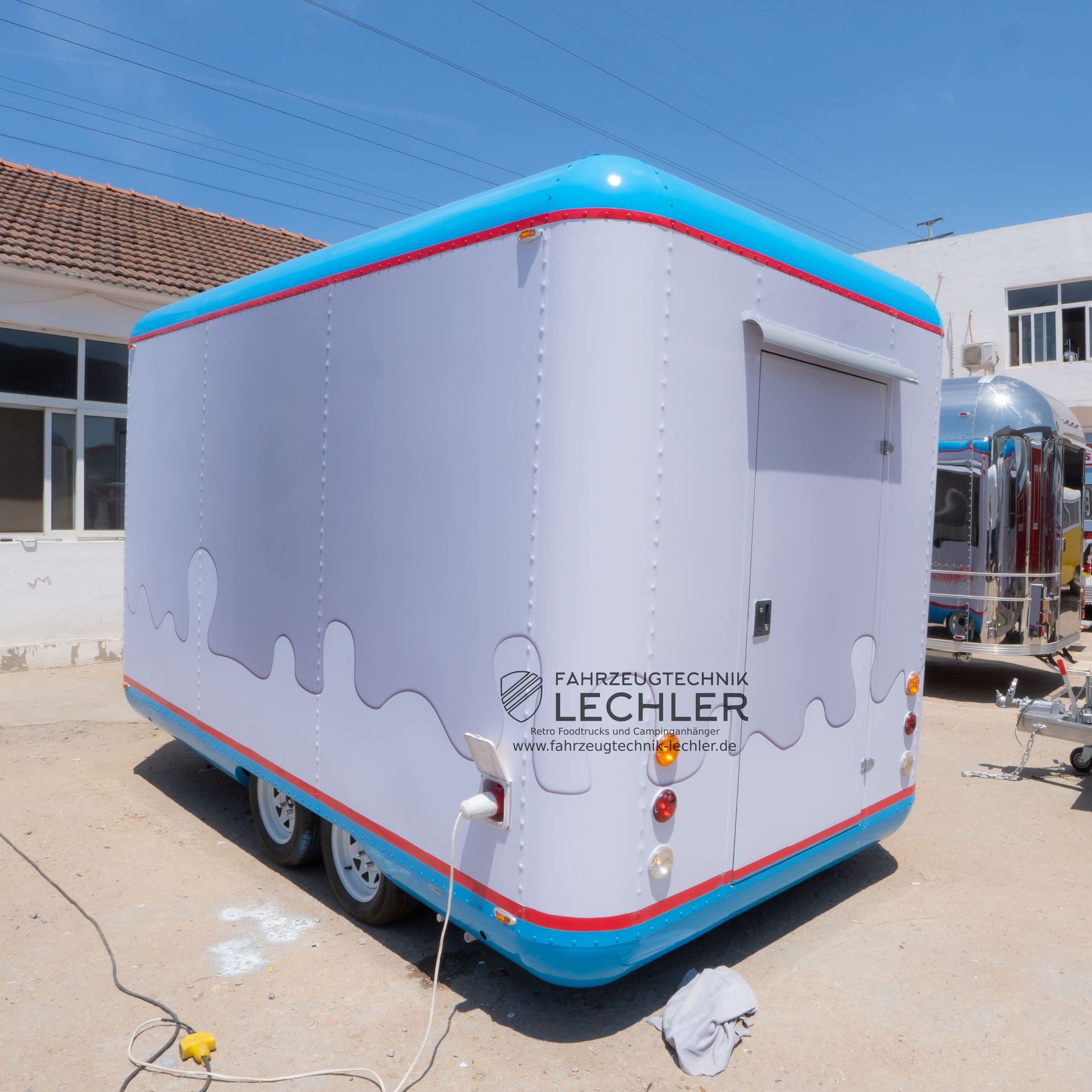 Aufblasbarer Imbisswagen mit blau-roten Zierelementen, weißer Außenfarbe und Logo, im Freien geparkt.