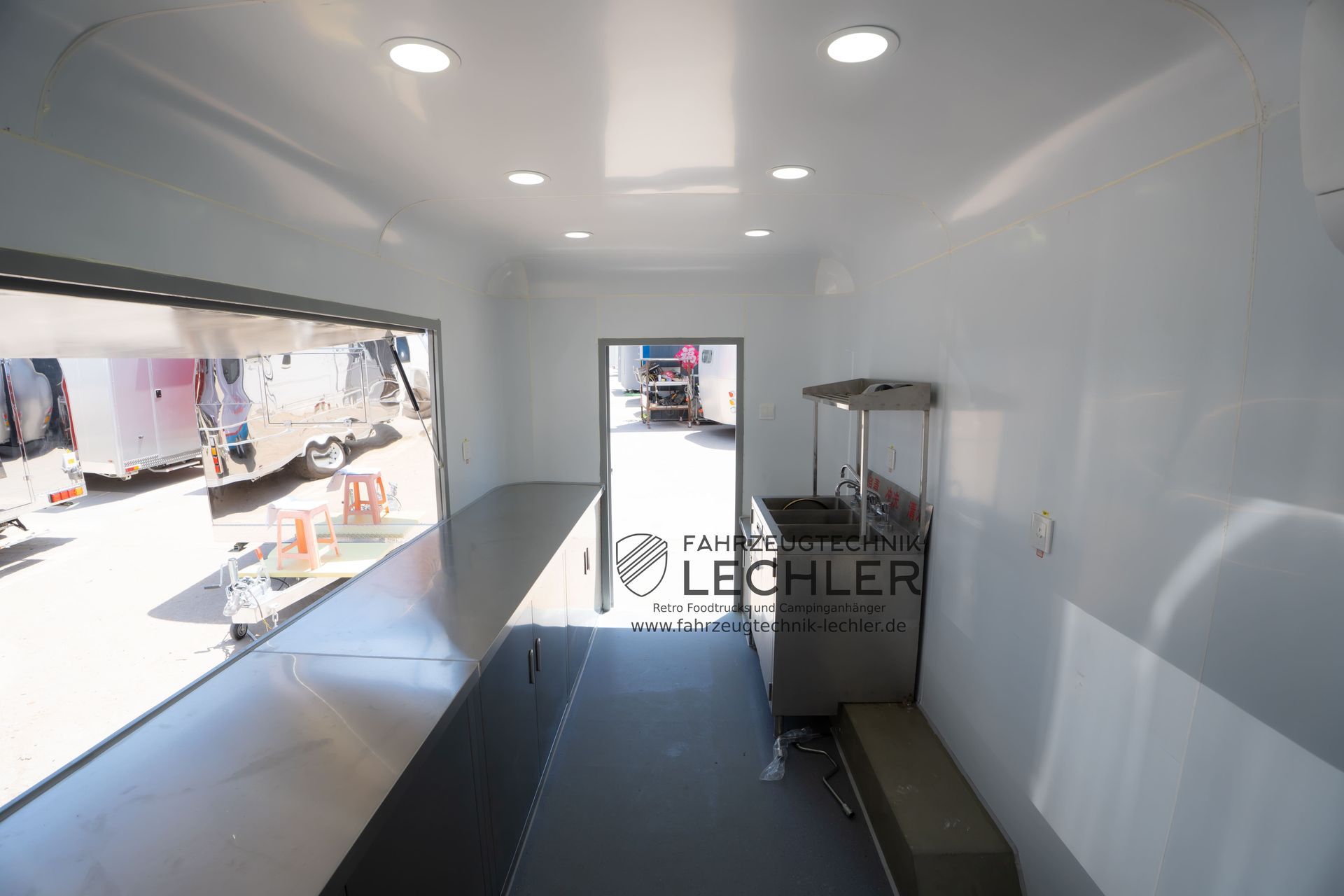 Innenansicht eines Imbisswagens mit Arbeitsplatten aus Edelstahl, einem Ausgabefenster und industrieller Ausrüstung.