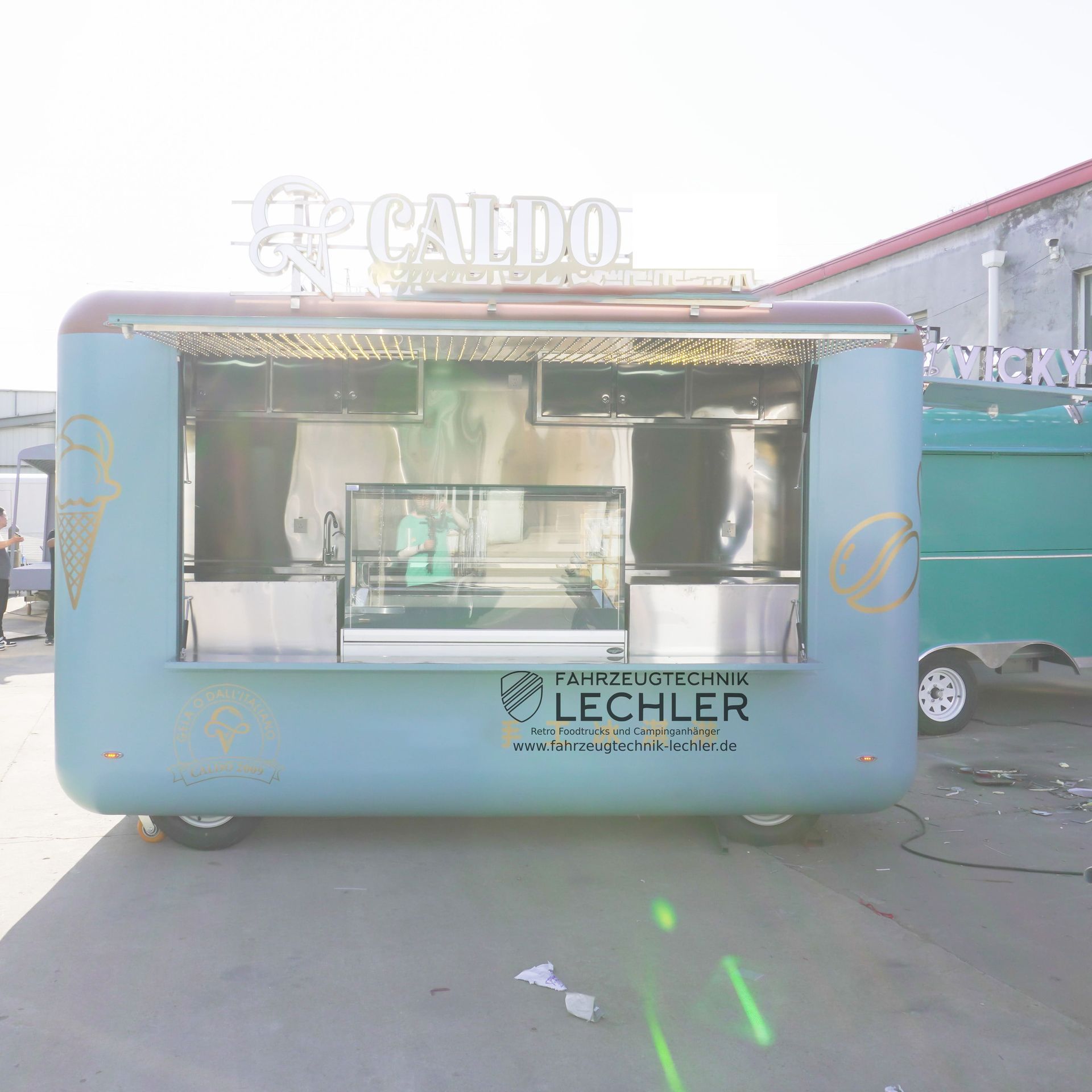 Blauer Imbisswagen mit Fenster, Logo und „Caldo“-Schild.