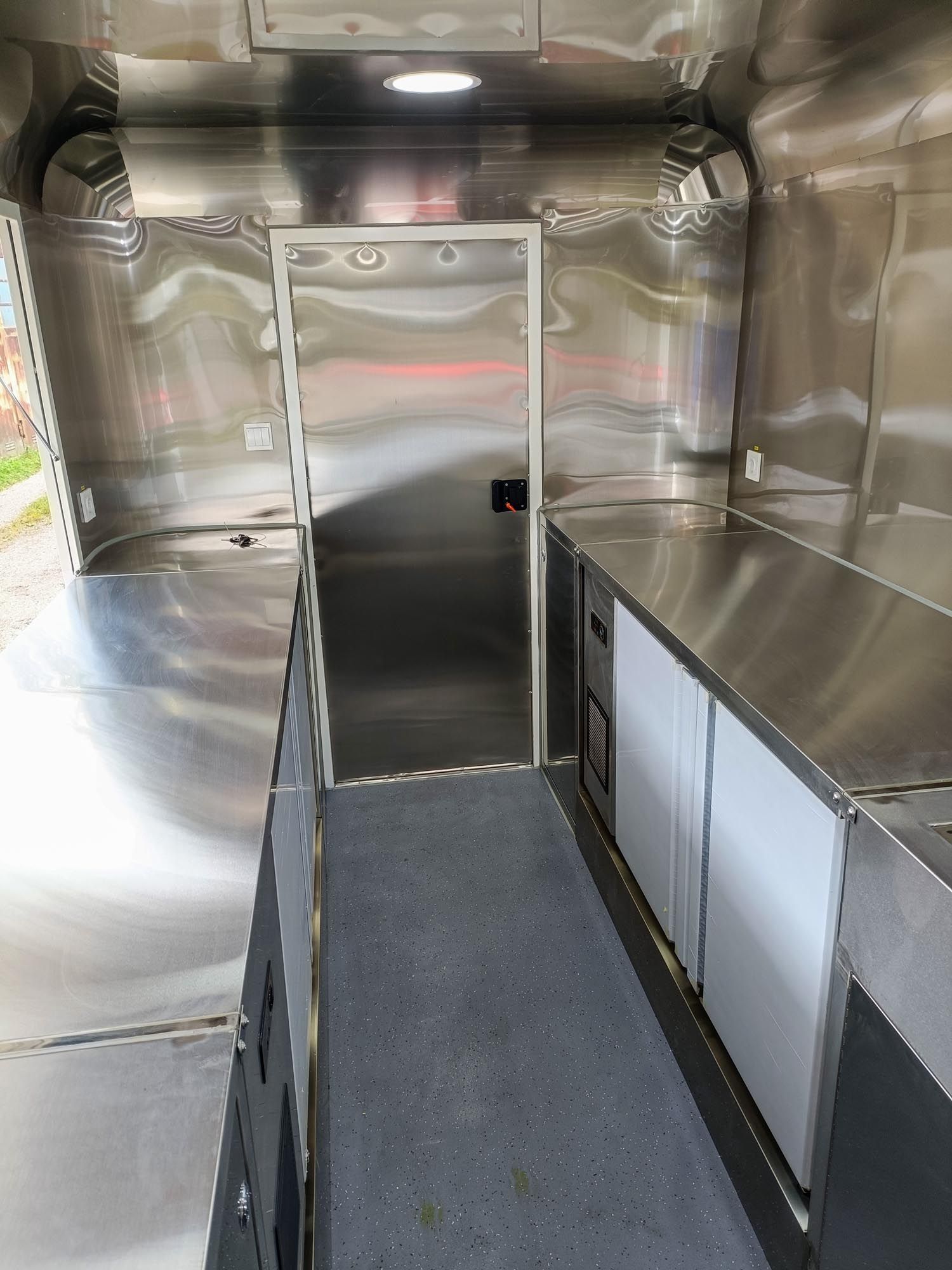 Innenansicht eines Imbisswagens. Theken und Wände aus Edelstahl, mit einem Kühlschrank und einer Tür in einem schmalen Raum.