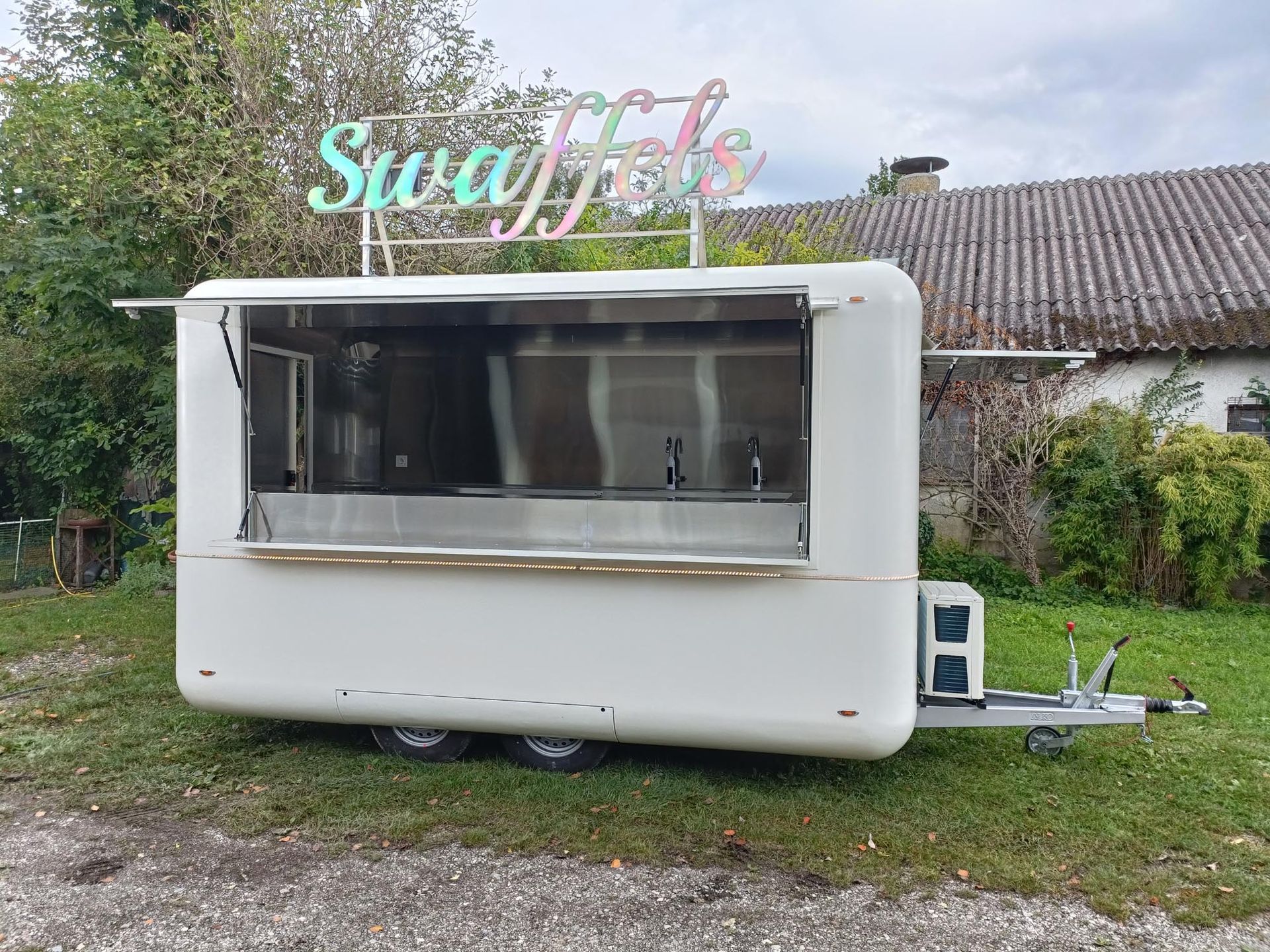 Weißer Imbisswagen mit dem Schild „Swaffels“ auf einer Rasenfläche.