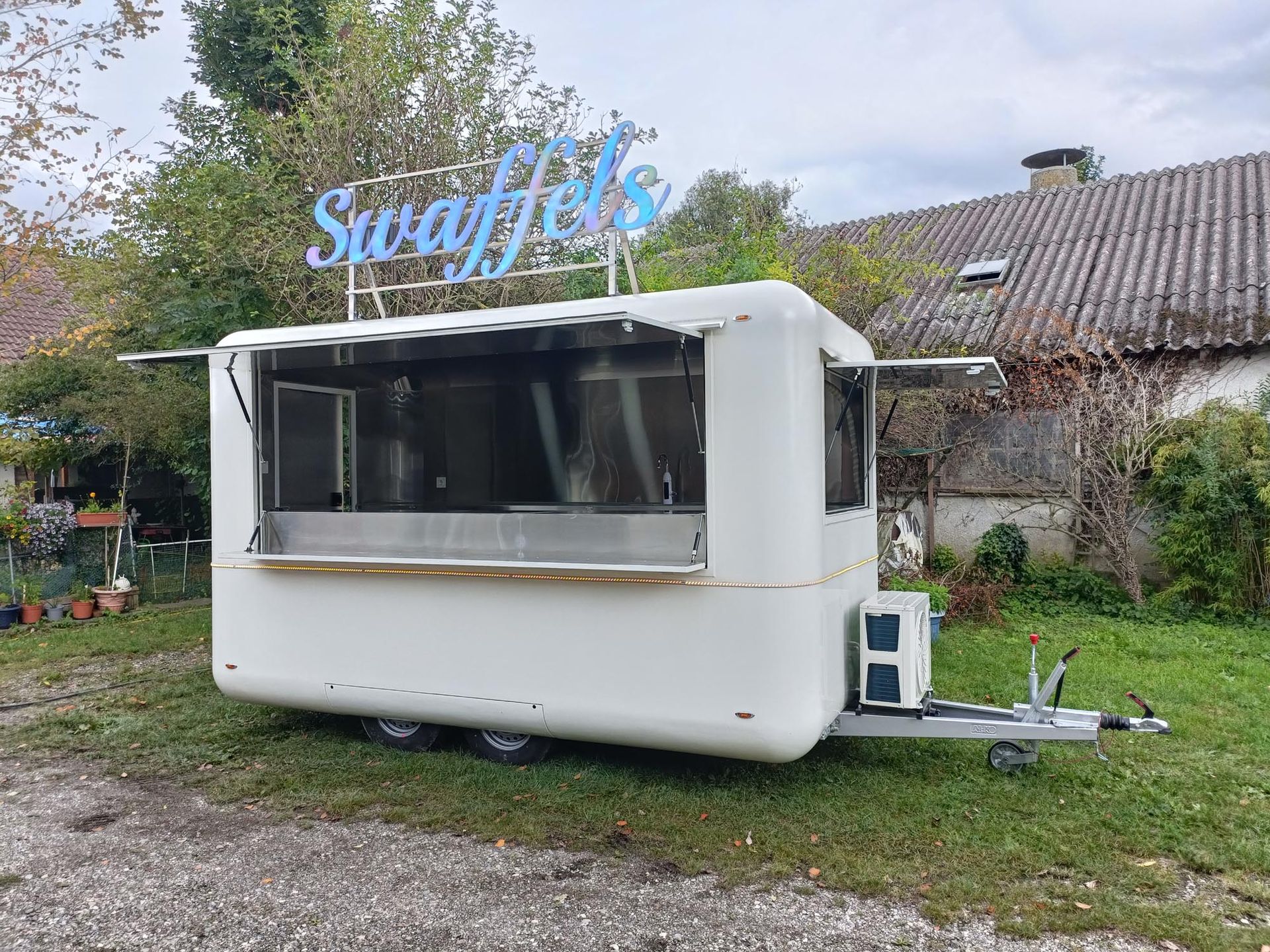 Weißer Imbisswagen mit dem Schild „Swaffles“, offene Ausgabefenster, auf Rasen.