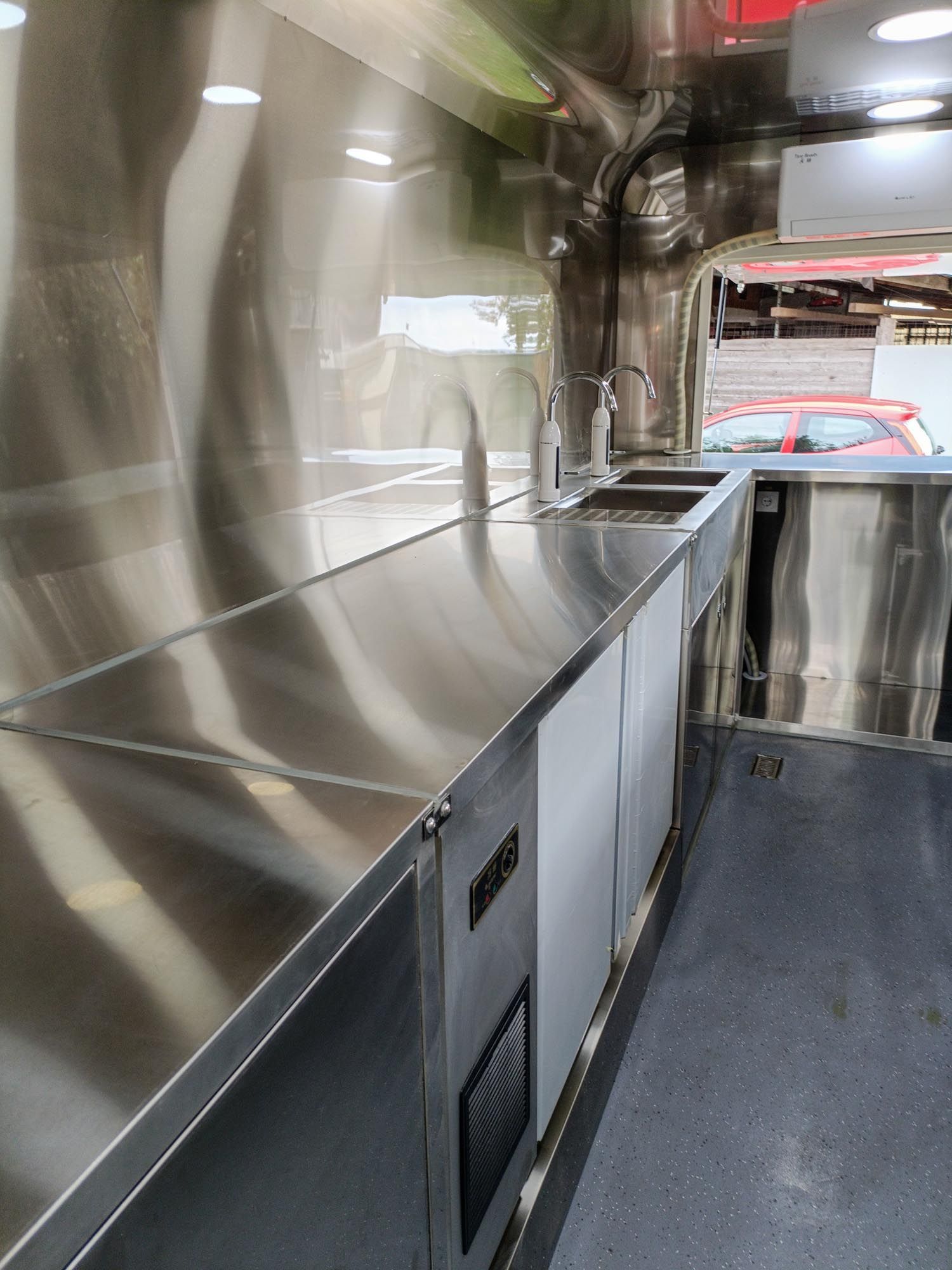 Innenansicht der Küche eines Imbisswagens aus Edelstahl mit Arbeitsflächen, Spülbecken und Geräten.