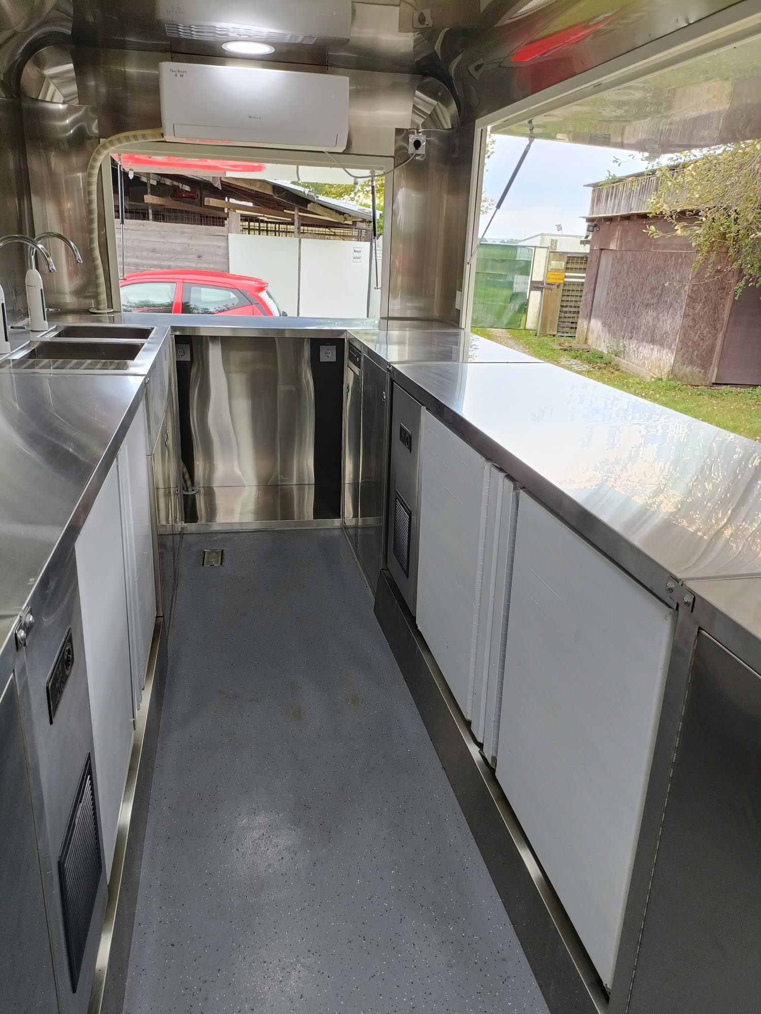 Innenansicht eines Imbisswagens aus Edelstahl mit Theken, Geräten und einem Fenster mit Blick nach draußen.