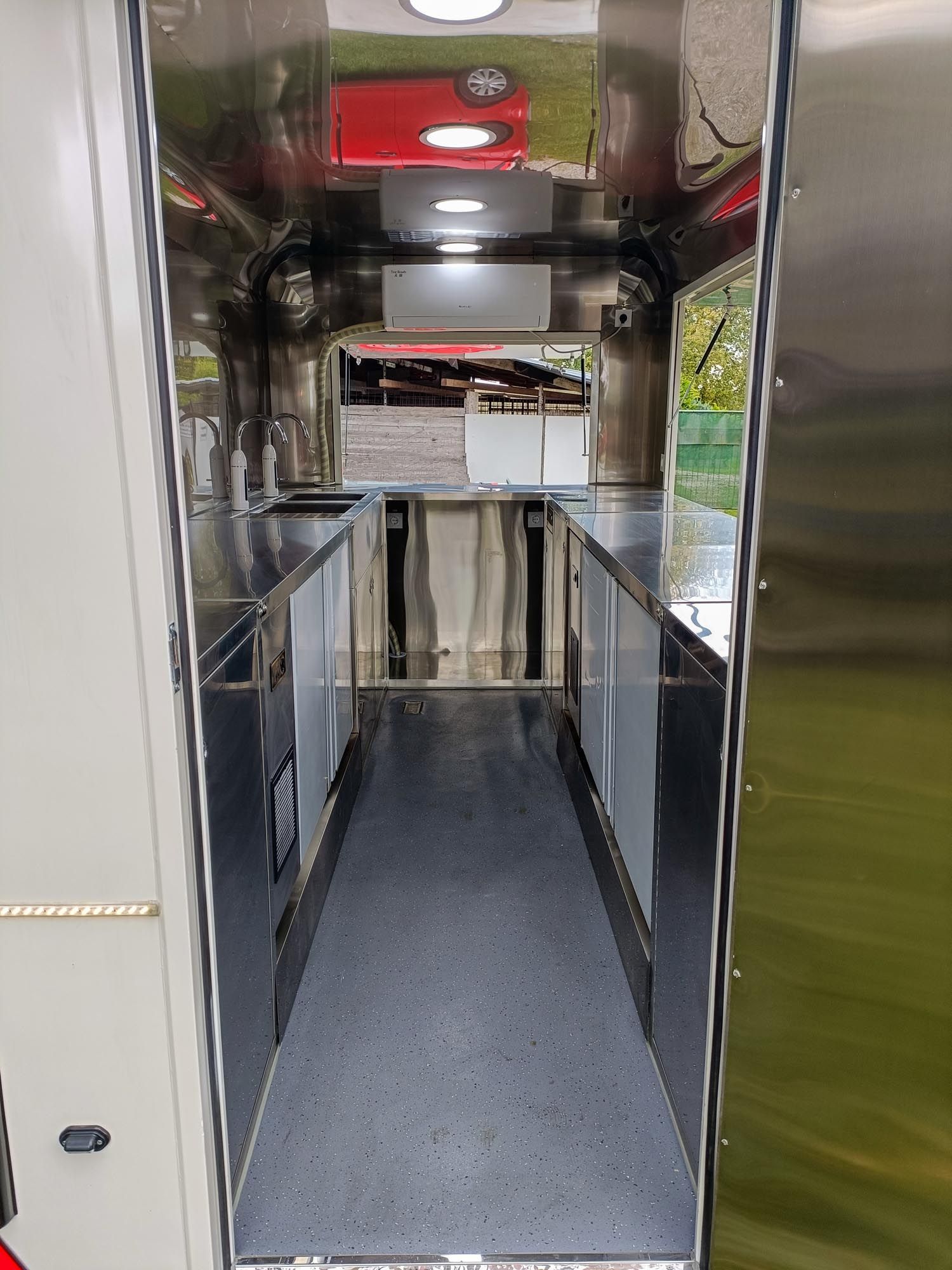 Innenansicht eines Imbisswagens. Edelstahltheken säumen die Seiten. Ein dunkler Boden führt zu einem offenen Ausgabefenster.