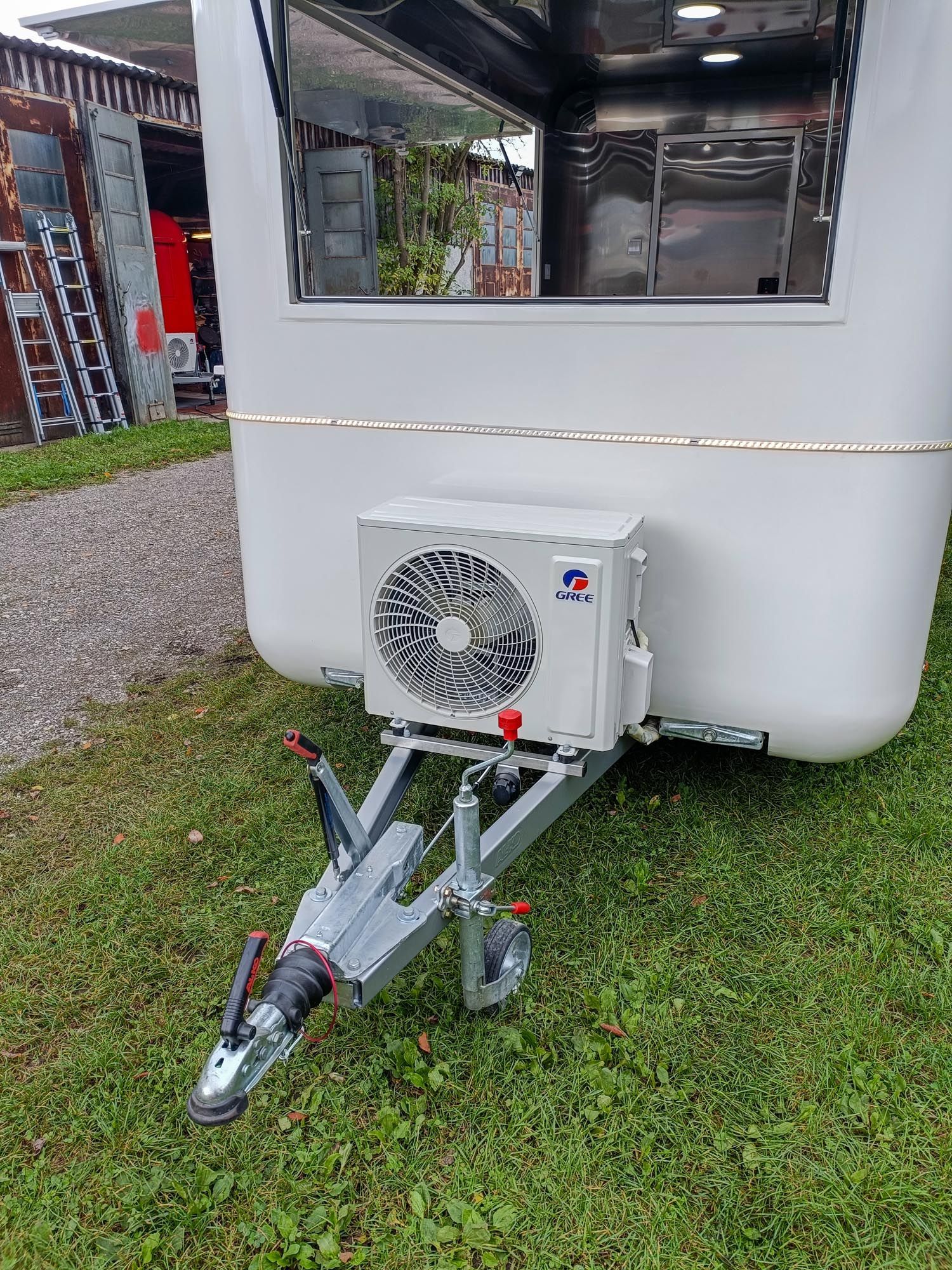 Weißer Imbisswagen mit vorne montierter Klimaanlage, geparkt auf einer Rasenfläche.