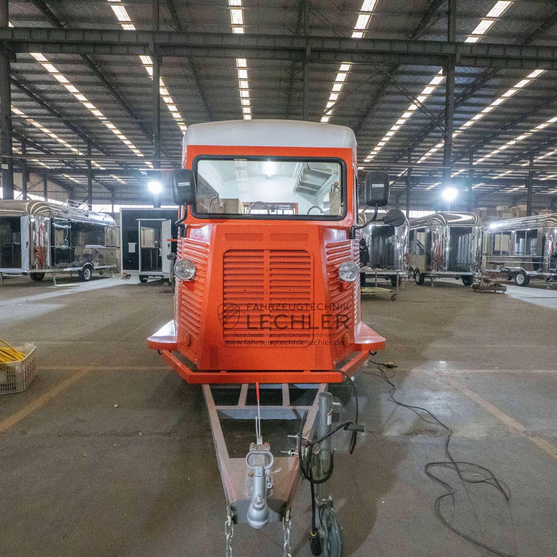 Oranger Imbisswagen mit weißem Dach und Anhängerkupplung in einer großen Lagerhalle.