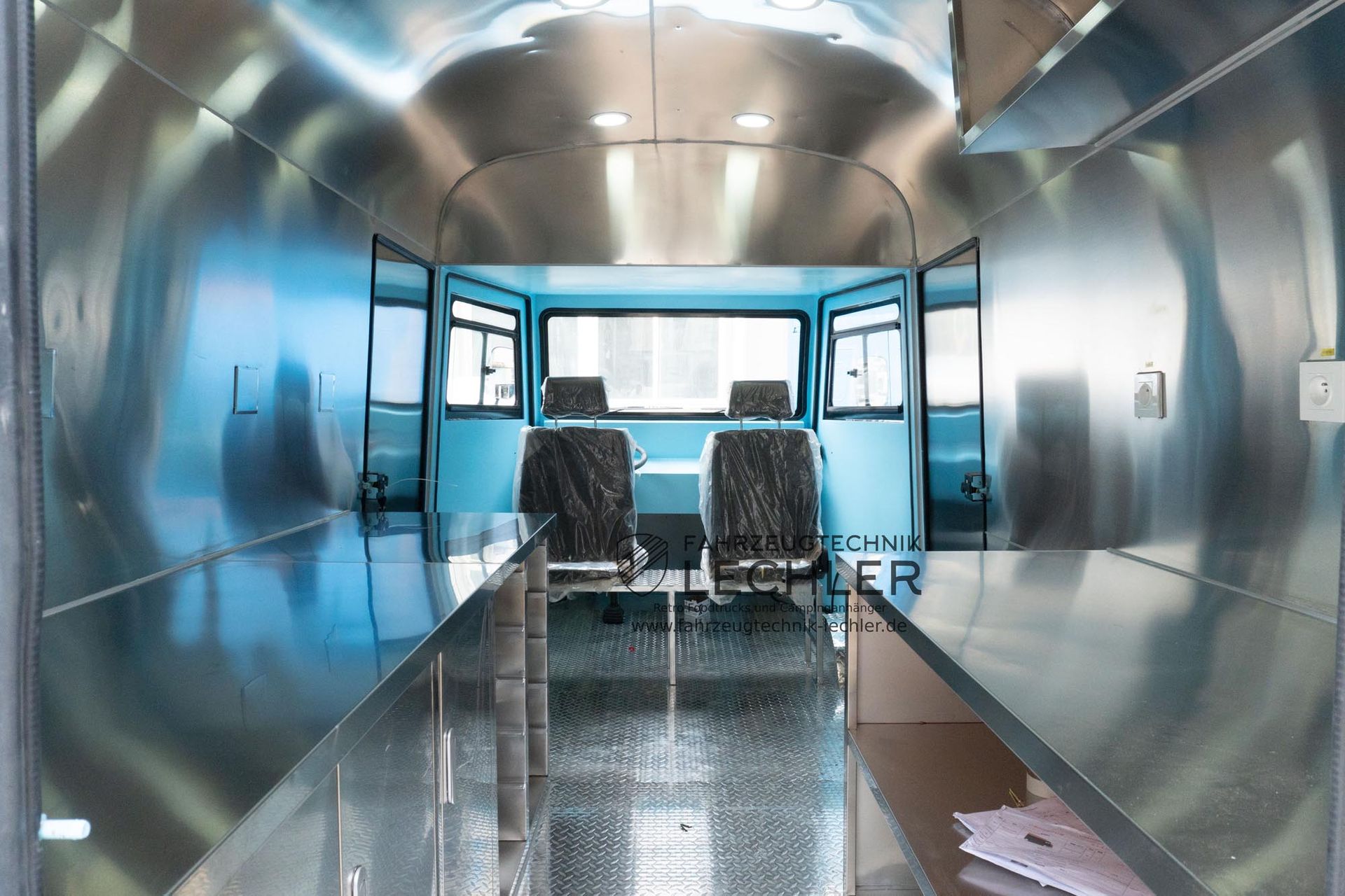 Innenraum eines Fahrzeugs mit Metallwänden, zwei Sitzen und Blick nach draußen. Blaue Akzente.