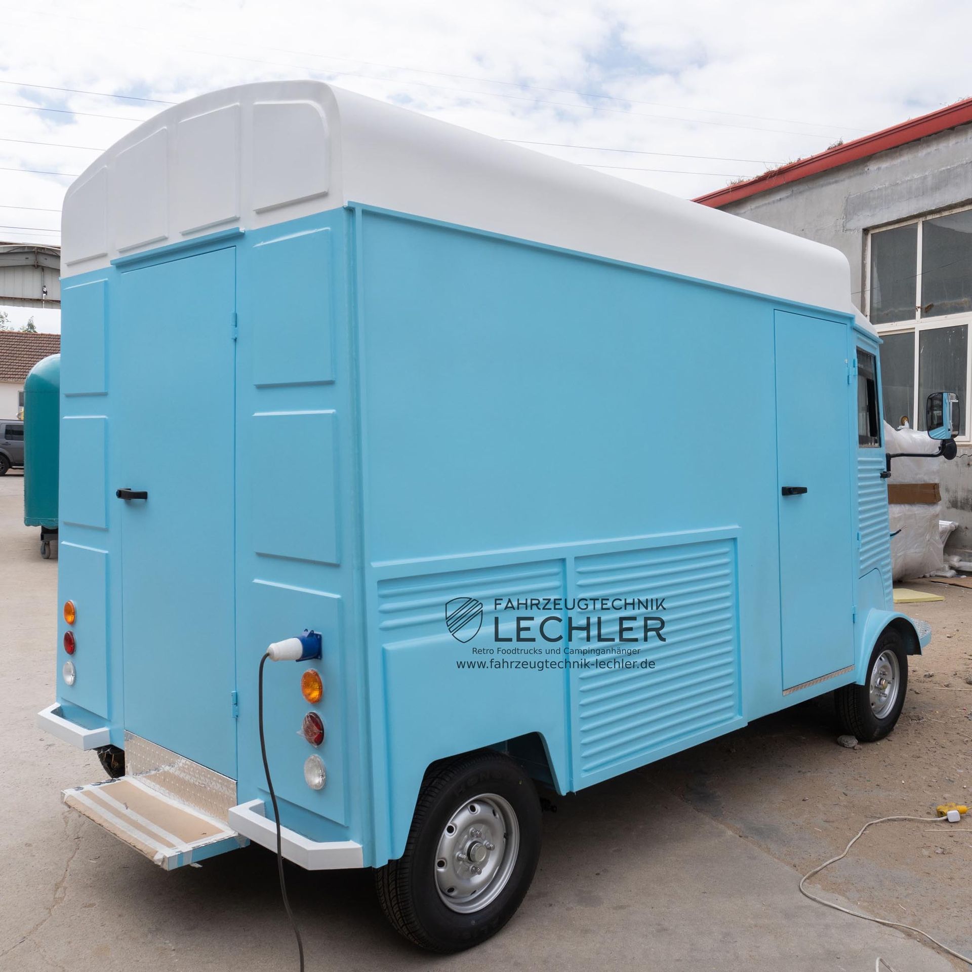 Hellblauer Imbisswagen mit weißem Dach, der gerade lädt, steht draußen.