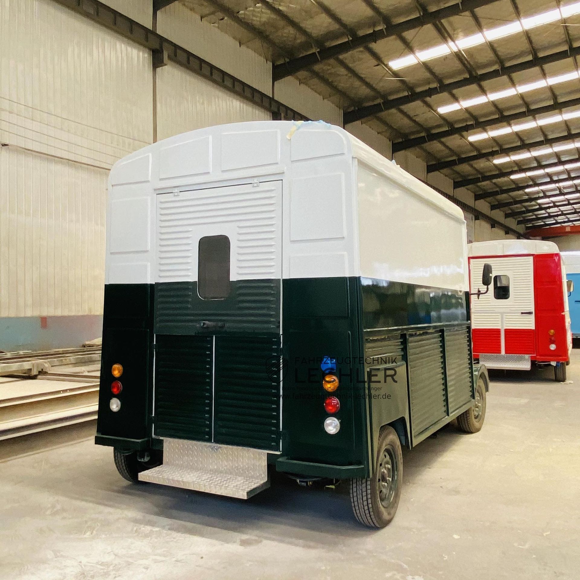 Rückansicht eines dunkelgrün-weißen Imbisswagens, der in einer Lagerhalle geparkt ist.