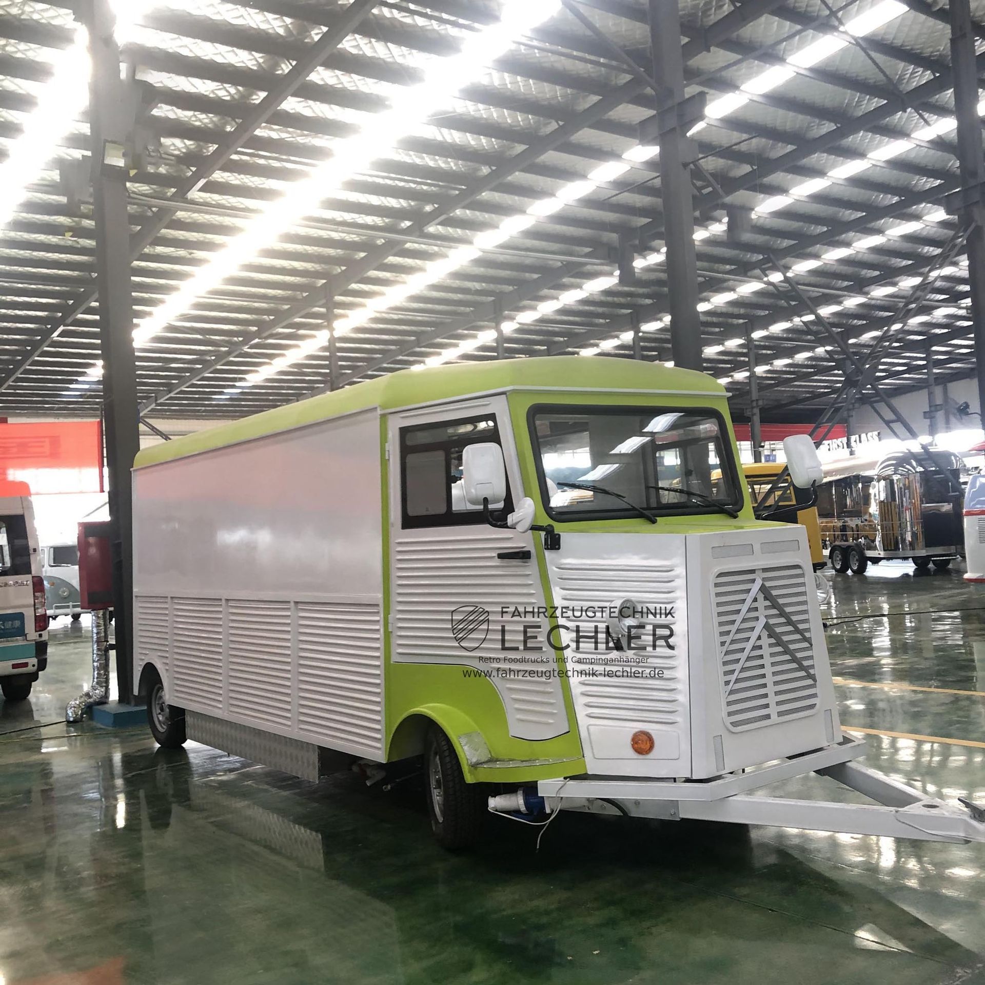 Ein Imbisswagen mit grün-weißer Außenfarbe steht in einer großen Lagerhalle.