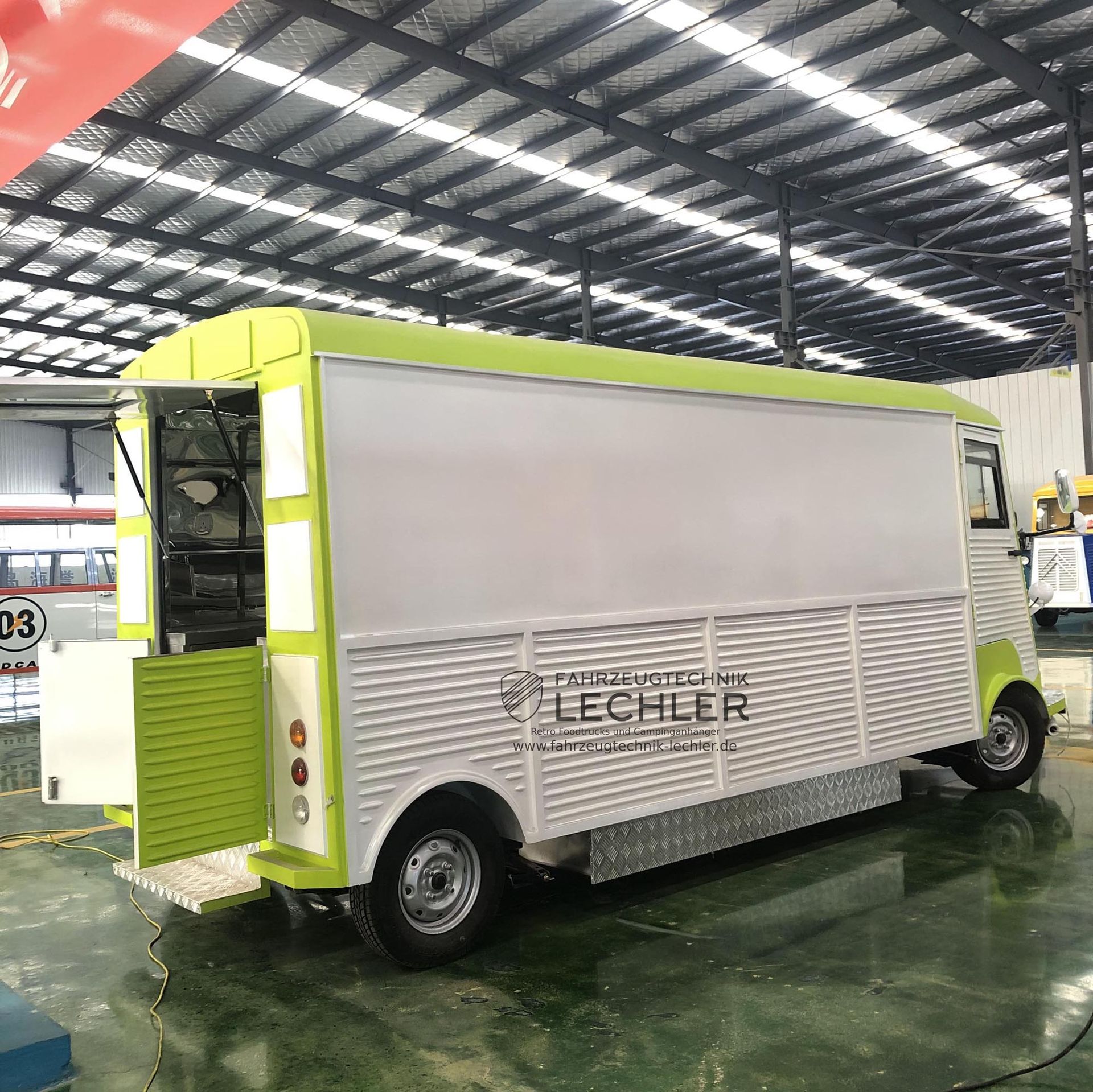 Grüner und weißer Imbisswagen mit offener Ausgabeklappe, in einer Halle geparkt.