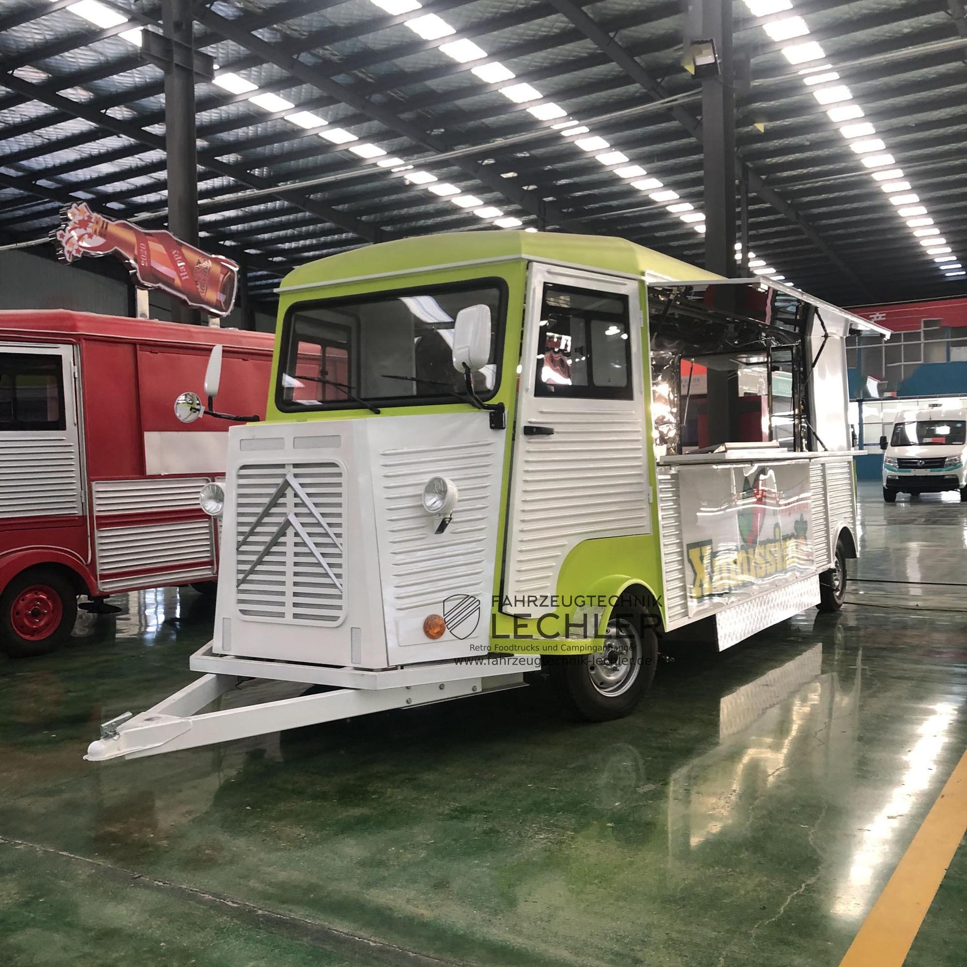 Ein Imbisswagen mit weiß-grüner Außenfarbe parkt in einer großen Lagerhalle.