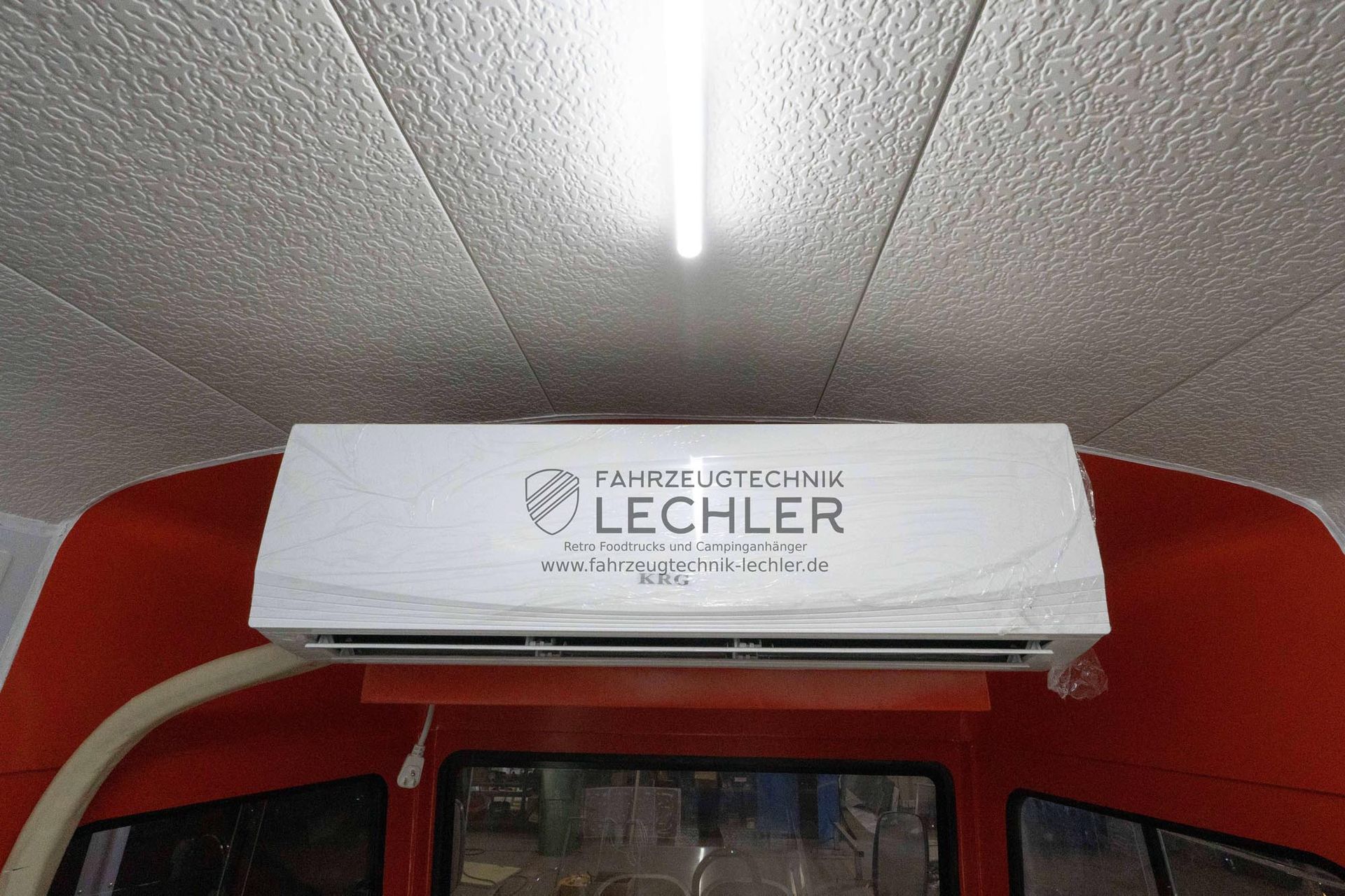 Klimaanlage in einem rot-weißen Lieferwagen. Auf dem Gerät ist „FAHRZEUGTECHNIK LECHLER“ aufgedruckt.
