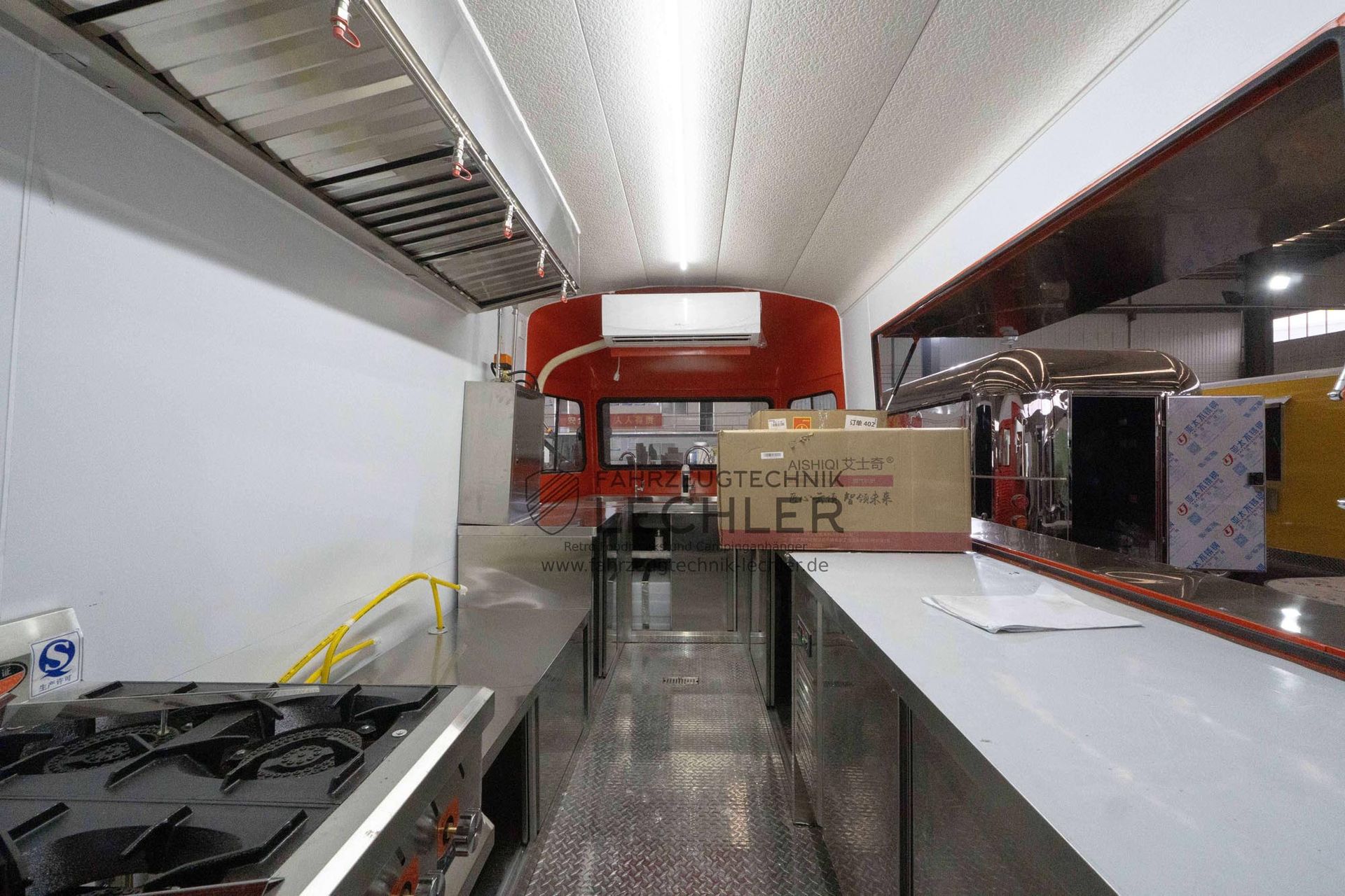 Innenansicht eines Imbisswagens. Arbeitsflächen, Kochfeld und Geräte aus Edelstahl. Rote Akzente und eine Kiste mit der Aufschrift „KOHLER“.
