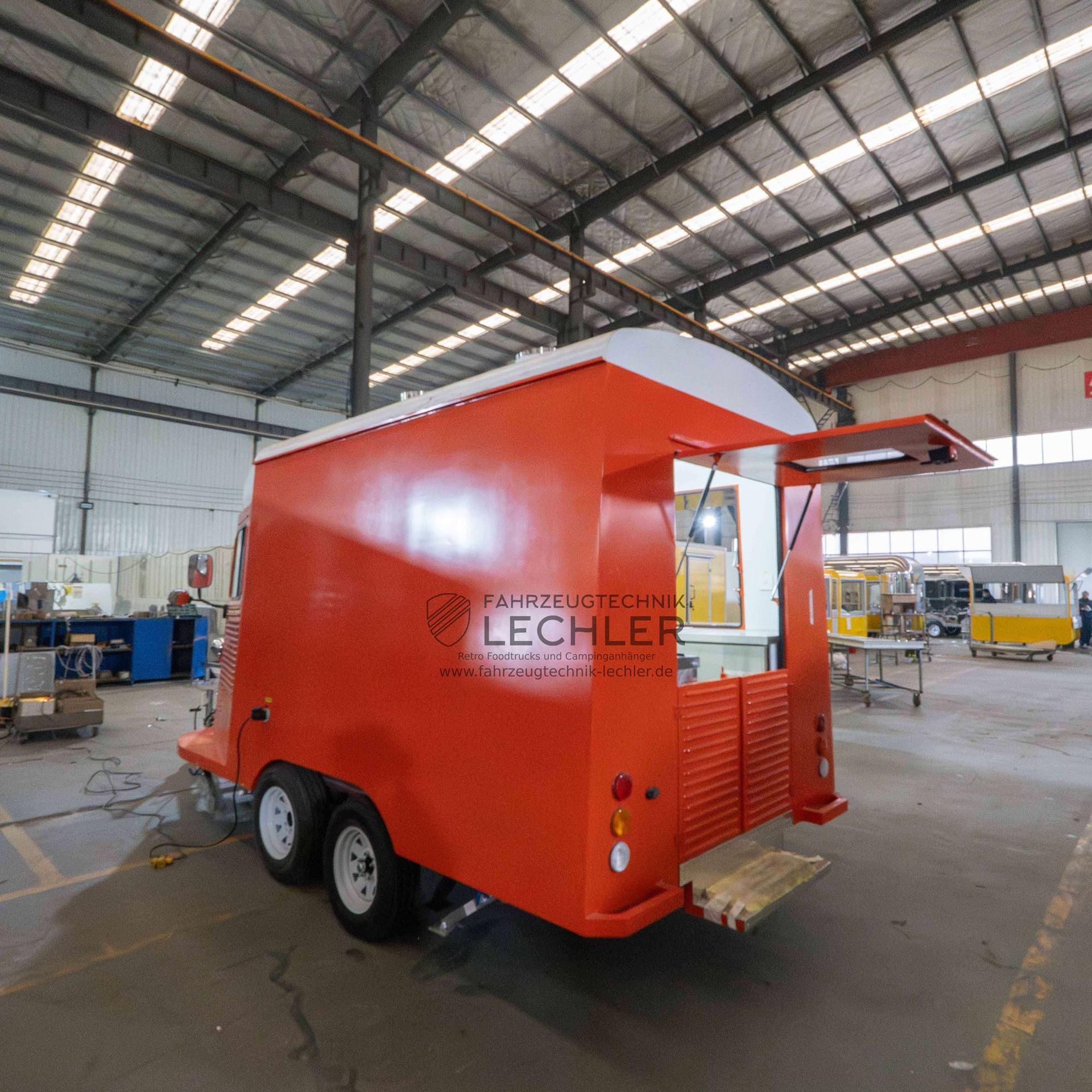 Oranger Imbisswagen mit offenem Ausgabefenster und weißen Rädern, geparkt in einer Lagerhalle.