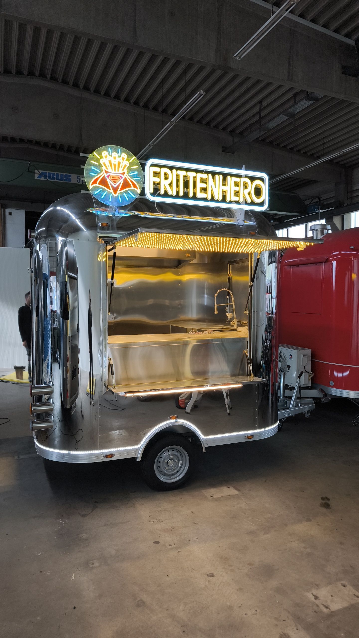 Glänzender silberner Imbisswagen mit dem Schild „FRITTENHERO“ und offenem Bedienungsfenster.