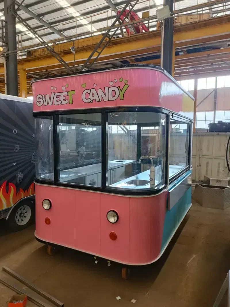Ein rosafarbener und türkisfarbener Imbisswagen der Marke „Sweet Candy“ mit großen Glasfenstern in einer Lagerhalle.