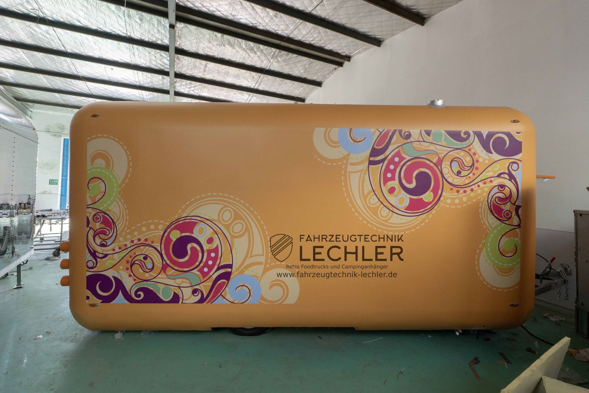 Gelbe aufblasbare Werbestruktur mit farbenfrohen Blumenmotiven und Firmenlogo in einer Lagerhalle.