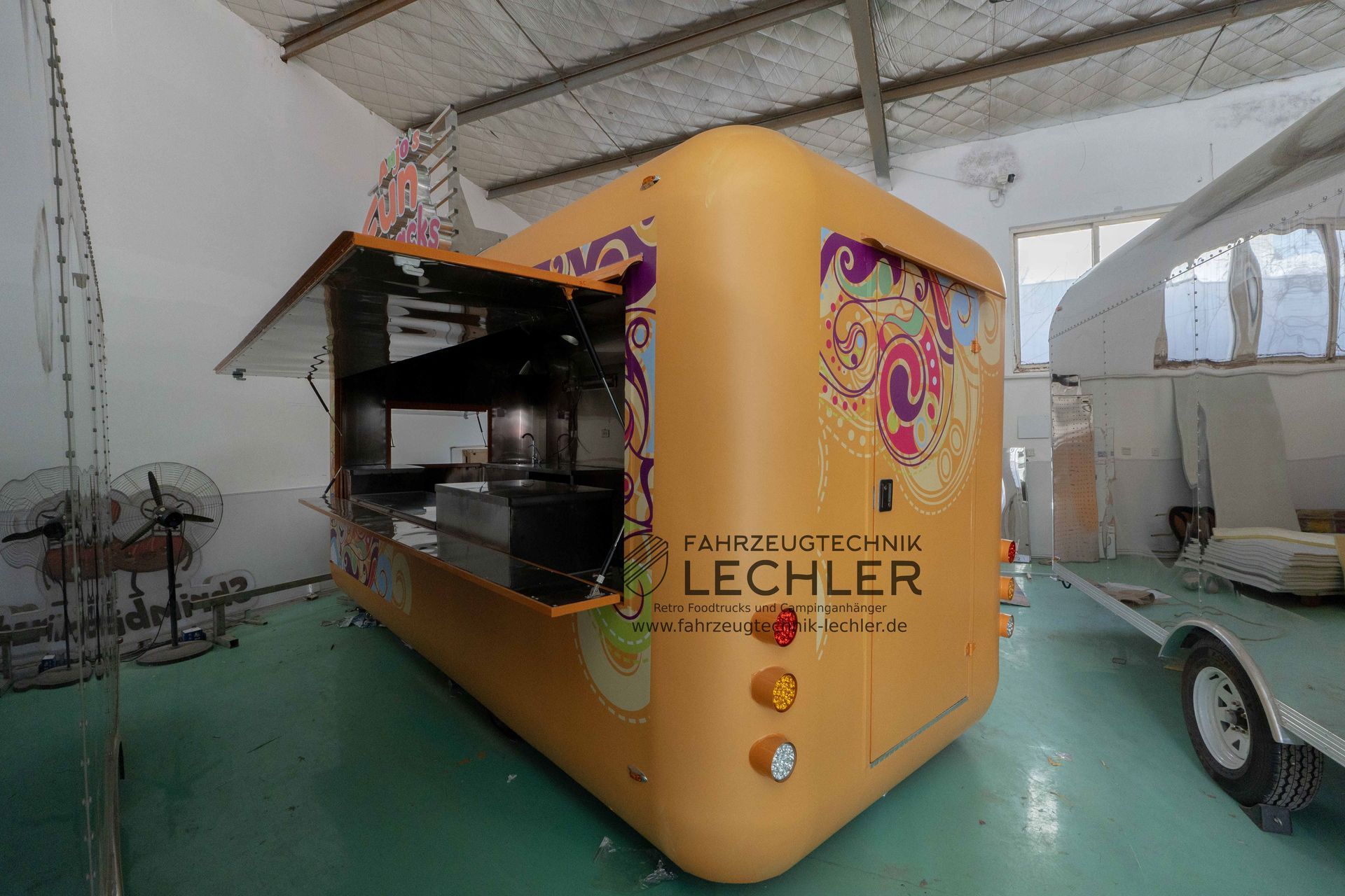 Gelber Imbisswagen mit offenem Ausgabefenster in einer Lagerhalle.