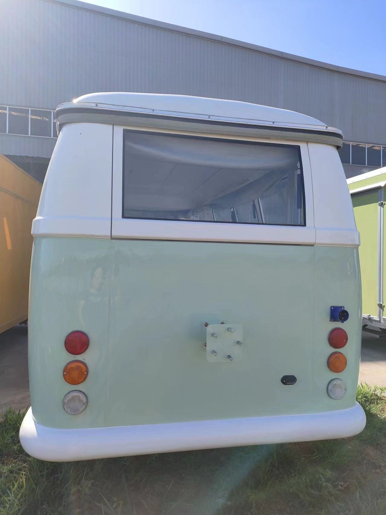 Rückansicht eines mintgrünen und weißen Wohnmobils im Vintage-Stil mit Fenster, Rückleuchten und Reserveradhalterung.